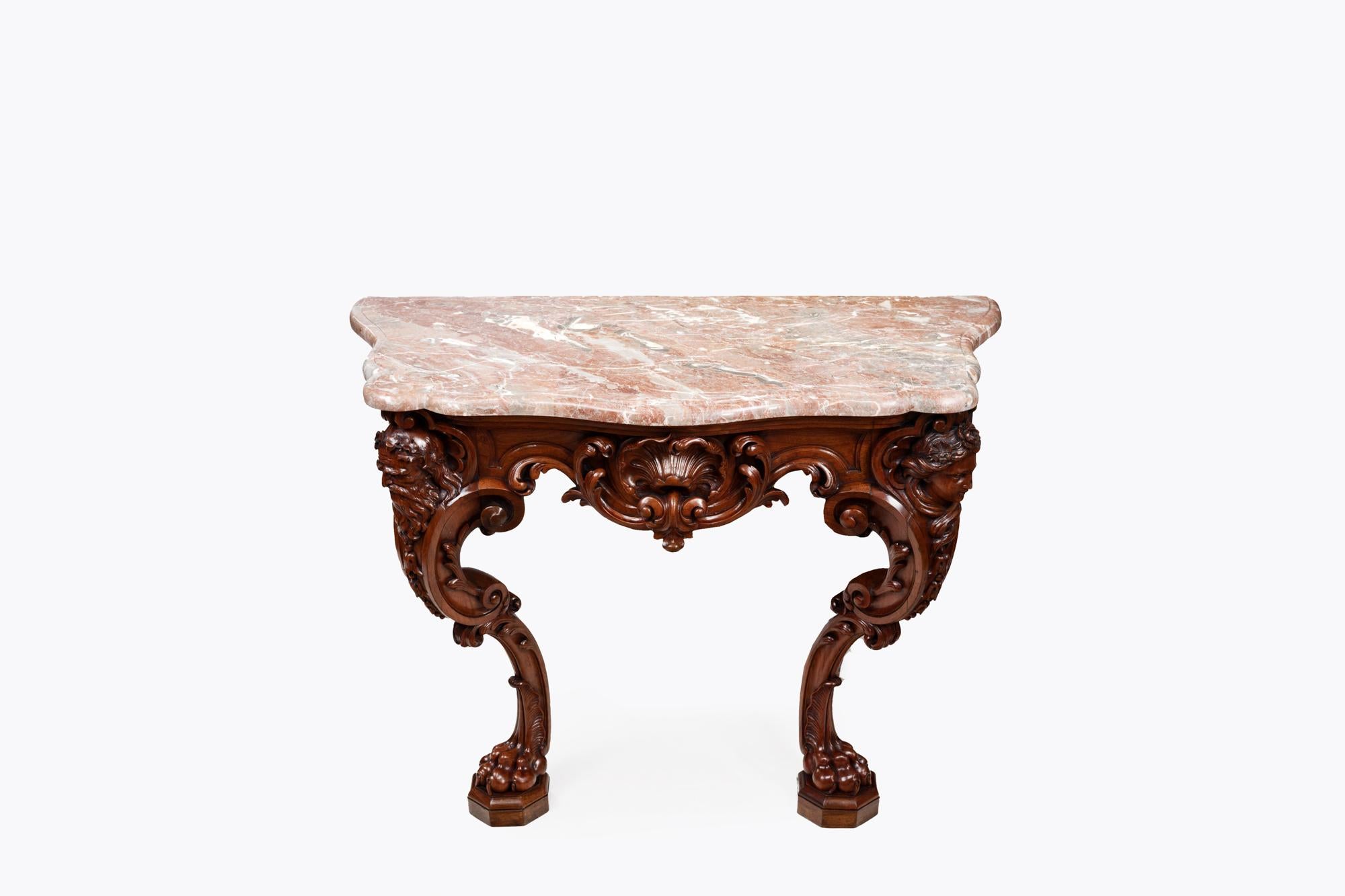 19th Century mahogany marble top serpentine console table. The red variegated top with moulded rim, above carved scrollwork base, the apron with central shell, flanked by male and female carved heads, raised on hairy lion paw feet with individual