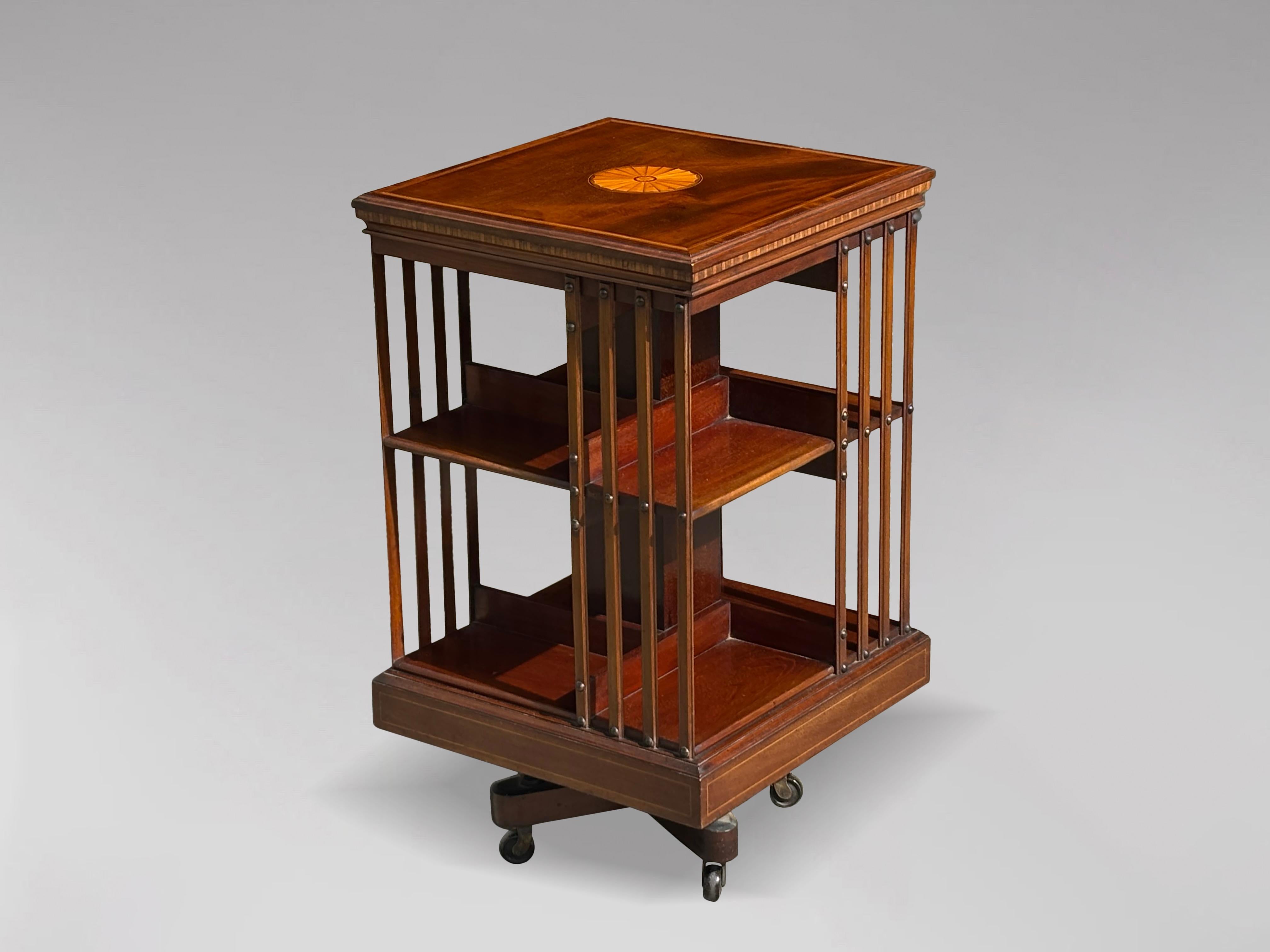 An attractive 19th century mahogany revolving bookcase with slatted sides, marquetry inlaid top with a chequered cross banded moulded edge, above two-tiered bookshelf with quarter sections divided by inlaid slats running from top to the base