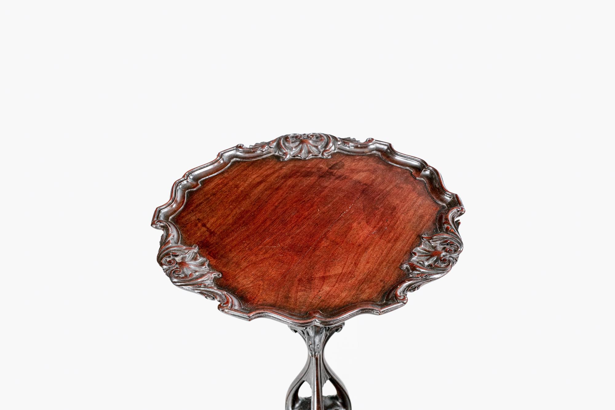 19th Century mahogany occasional table with carved circular top featuring a scallop edge with acanthus leaf design, raised on a profusely carved pierced tripod base supported by splayed legs terminating on pad feet.