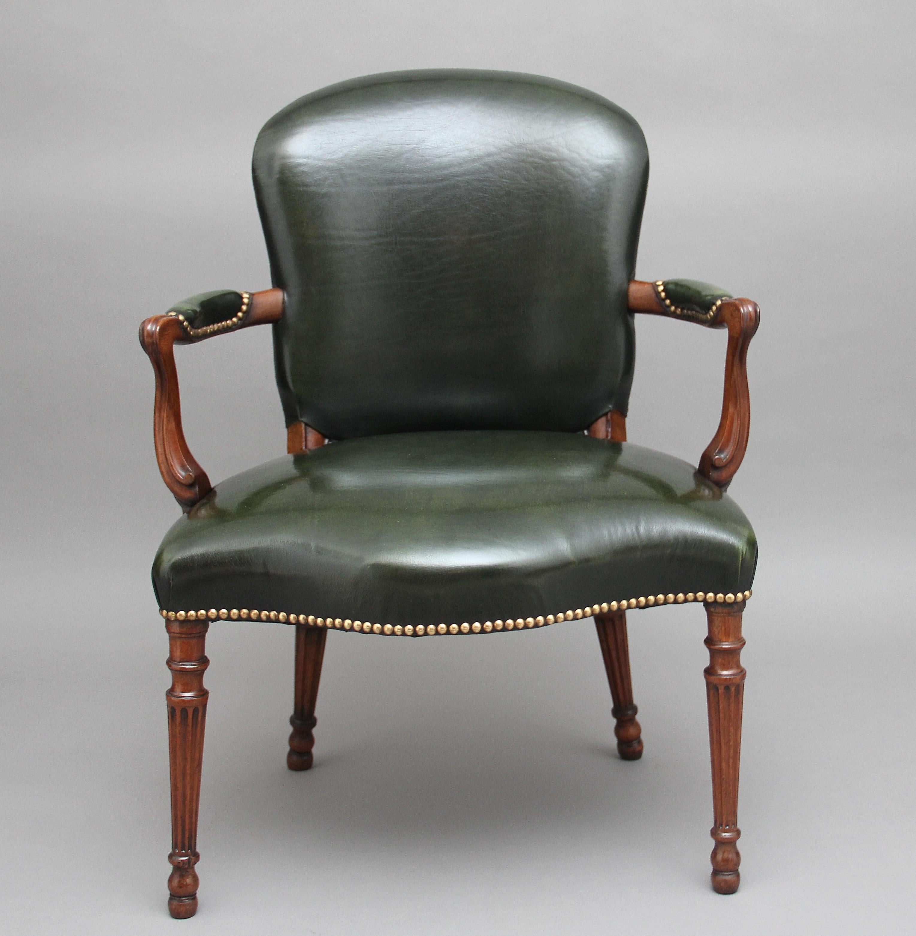 Early 19th century mahogany open armchair upholstered in green leather with brass stud decoration, standing on turned and fluted legs, a generous serpentine shaped seat with carved arms and shaped back, circa 1830.
 