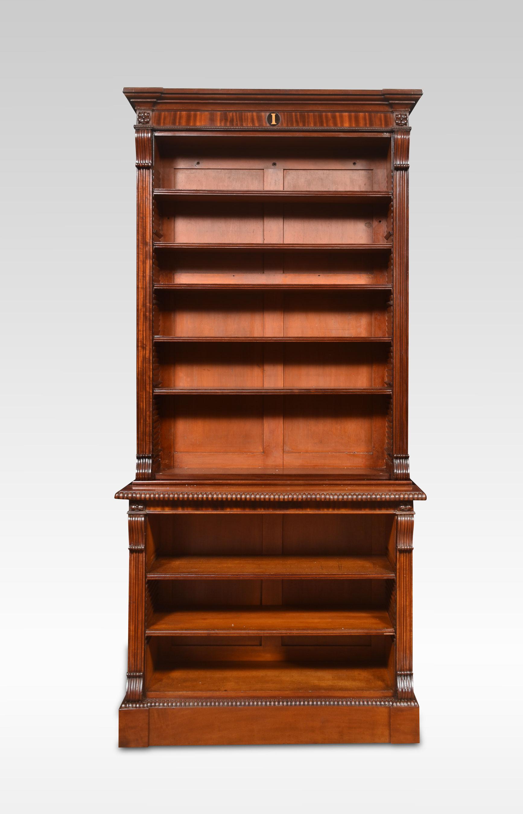 Large mahogany open bookcase, the carved moulded cornice with central ebony losange, above adjustable shelved interior. Flanked by carved reeded scrolling columns. All raised up on plinth base. The bookcase will separate into two sections for easy