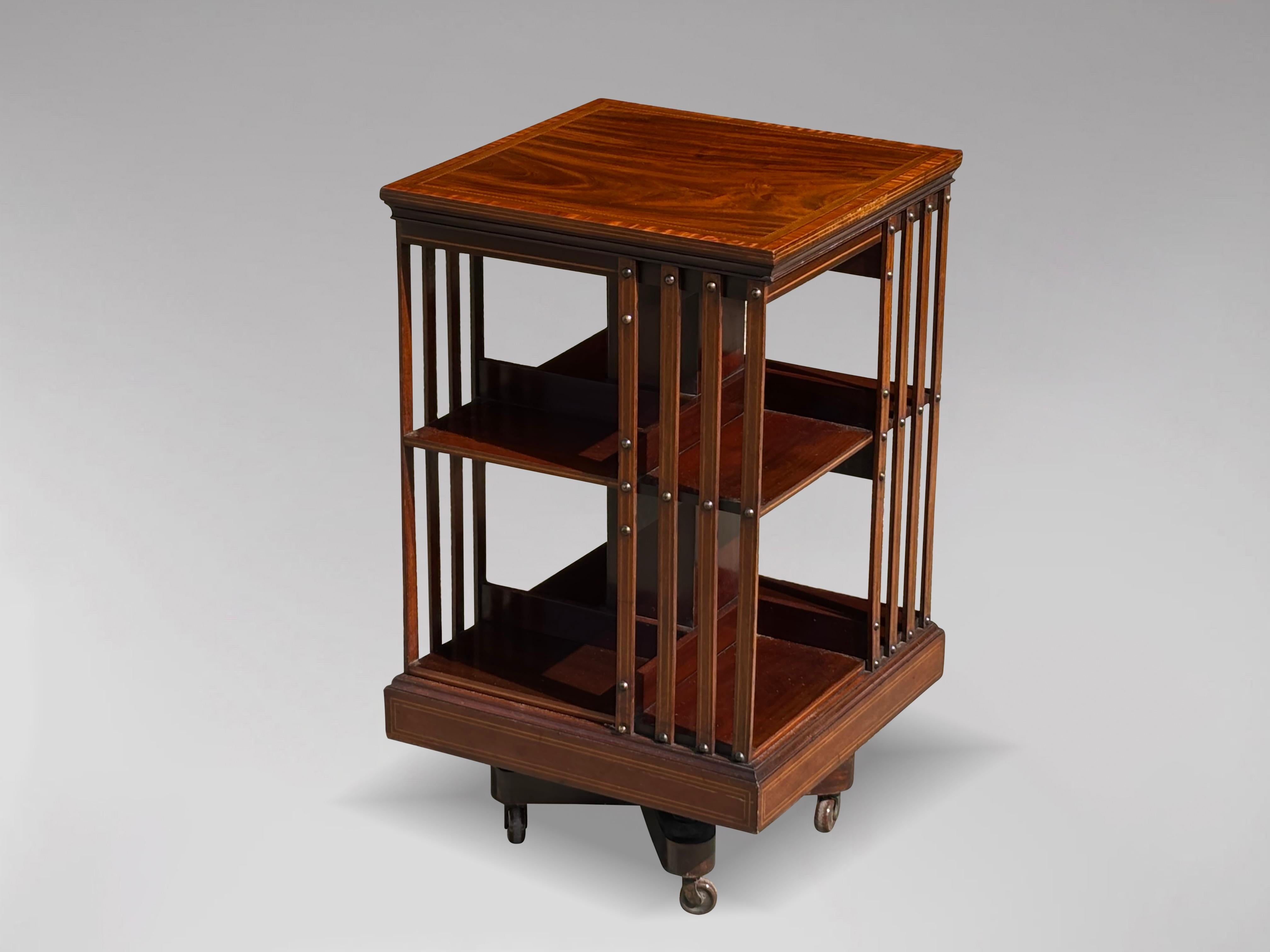 An attractive 19th century mahogany revolving bookcase with slatted sides, marquetry and crossbanded inlaid top, moulded edge, above two-tiered bookshelf with quarter sections divided by inlaid slats running from top to the base fastened with brass