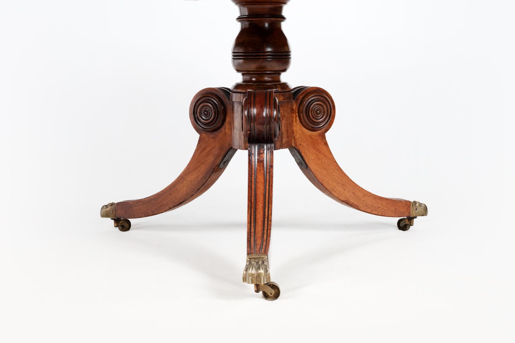 19th century mahogany tip-up dining table crossbanded with rosewood on splay pod legs terminating with brass lion feet castors.