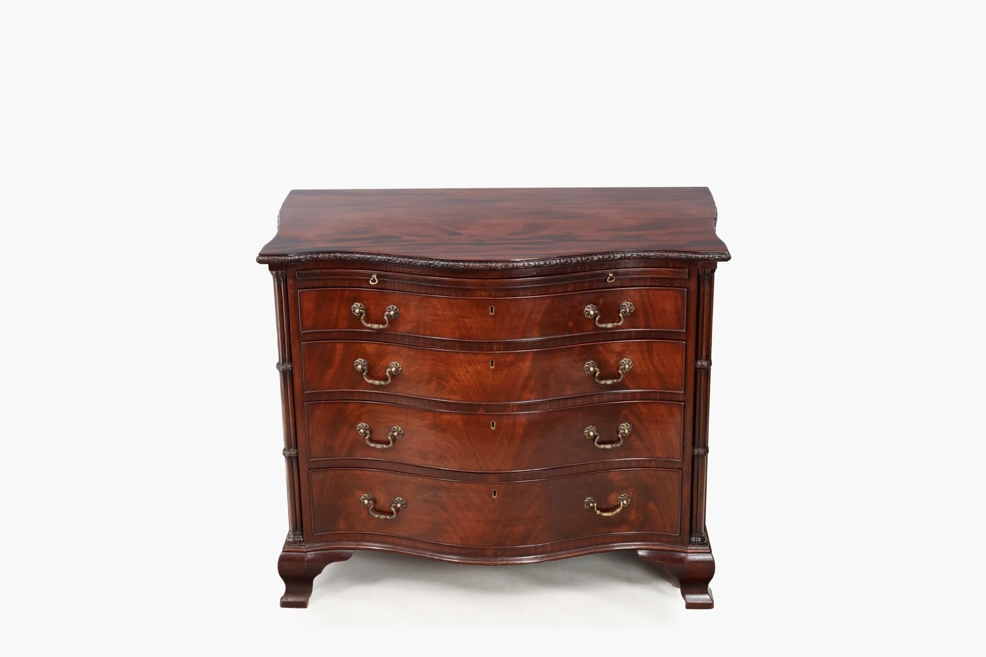 19th Century mahogany serpentine chest of drawers with carved molded top edge and cluster column detail. A full-length brush slide sits above four long drawers which are flanked on either end by the carved cluster columns. The piece is complete with