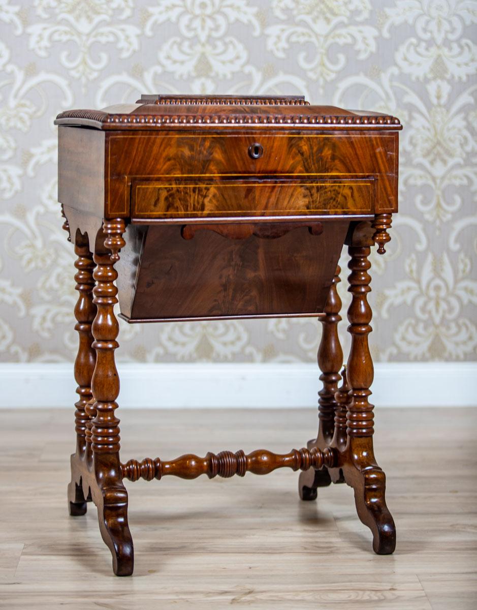 We present you a mahogany sewing table from the second half of the 19th century.
The apron is rectangular, with a liftable board, a storage compartment, and two drawers – one narrower and the other one in the shape of a cone, suspended at the