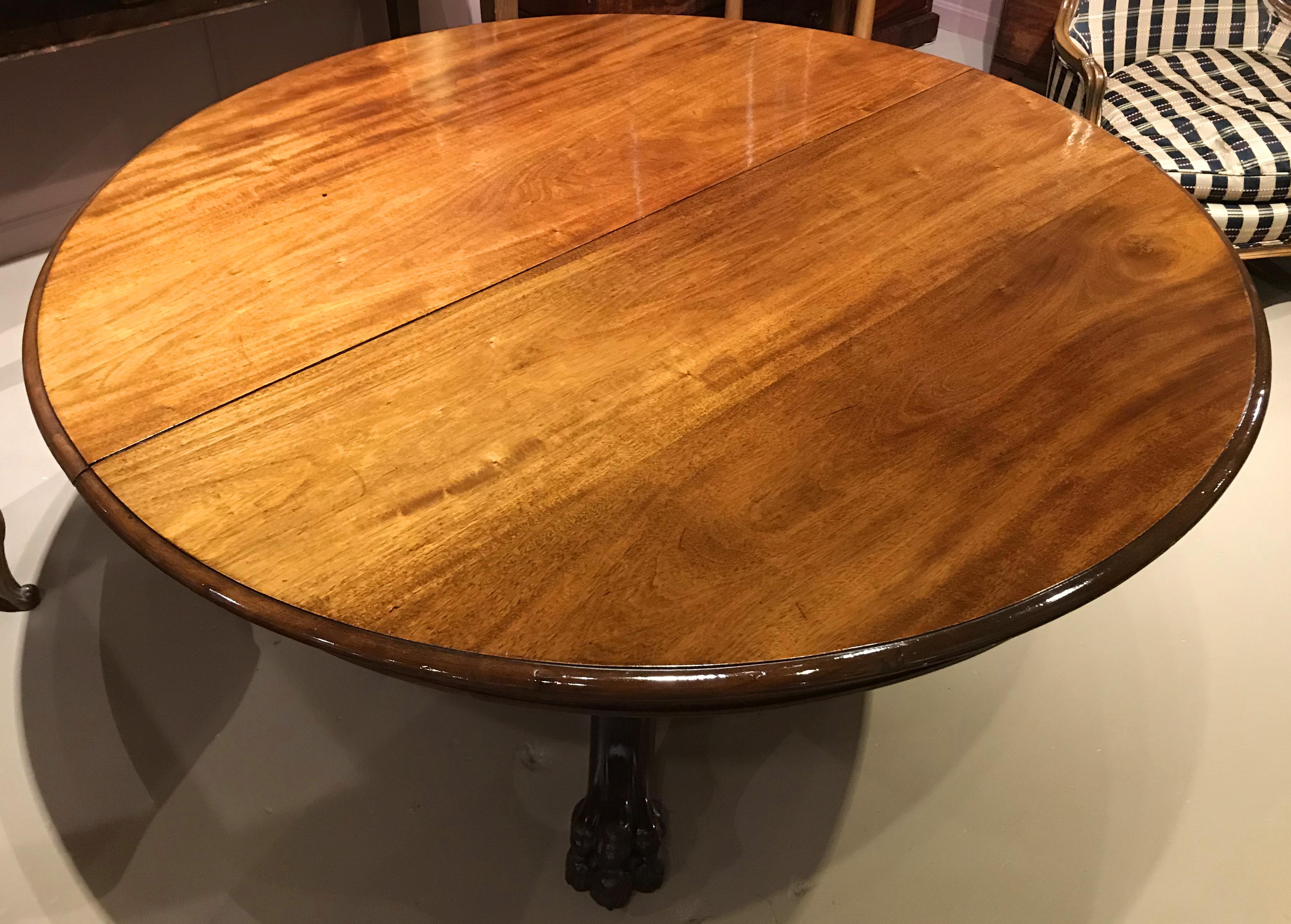 A fine mahogany split pedestal round dining table with gadrooned edge, paw feet, and three leaves. Pedestal opens to reveal center support leg and leaf support mechanism.Overall very good condition with some finish inconsistencies, fade and