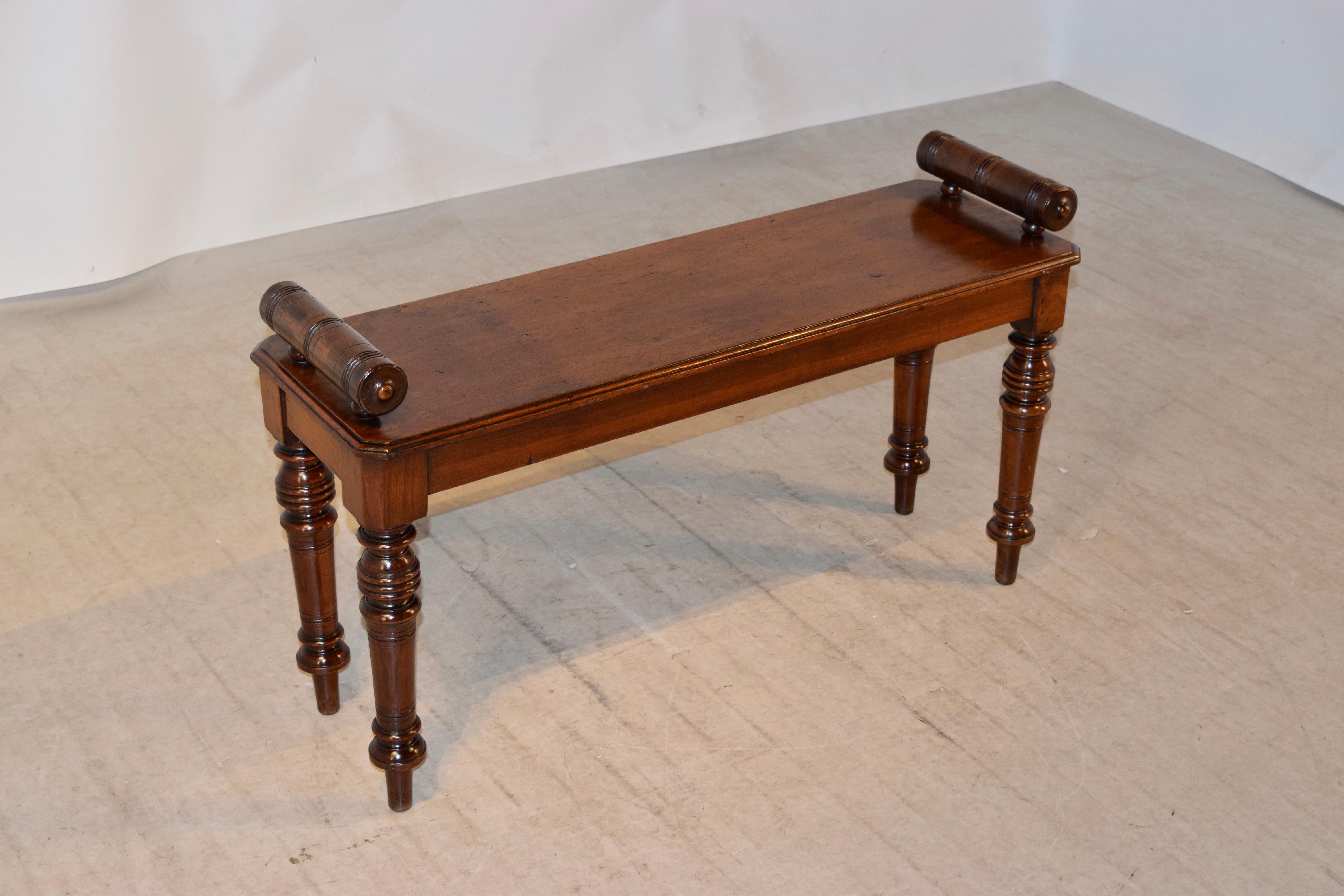 19th century English window seat made from mahogany with hand-turned rolled arms atop a single plank seat with beveled edges following down to a simple apron and supported on hand-turned legs.