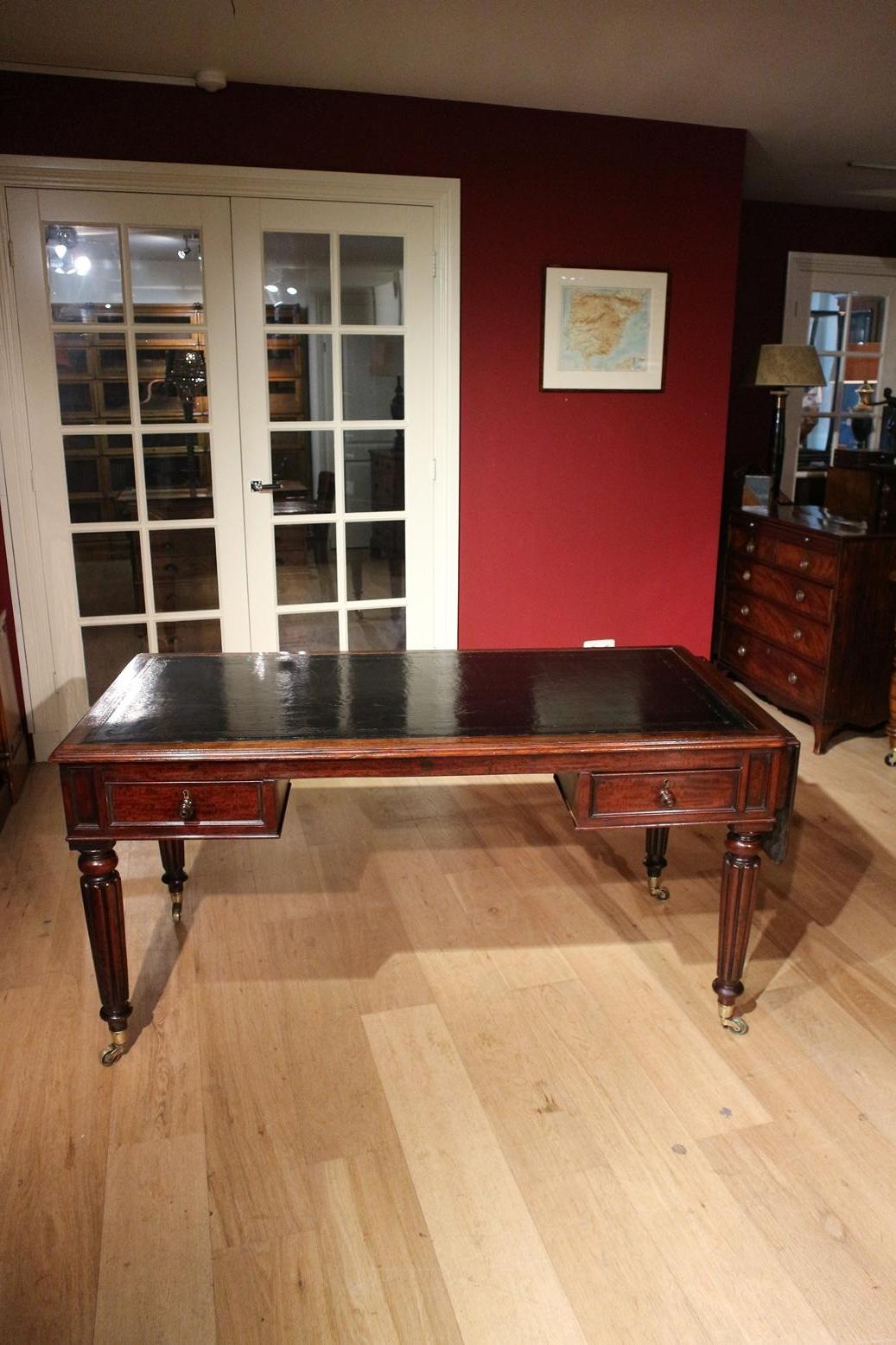 Early 19th century antique mahogany writing table. In very good condition. The table has as a special feature a fold-out leaf on the right. Very good quality table. The table has a stylish leg with branded brass wheels. The black leather top has