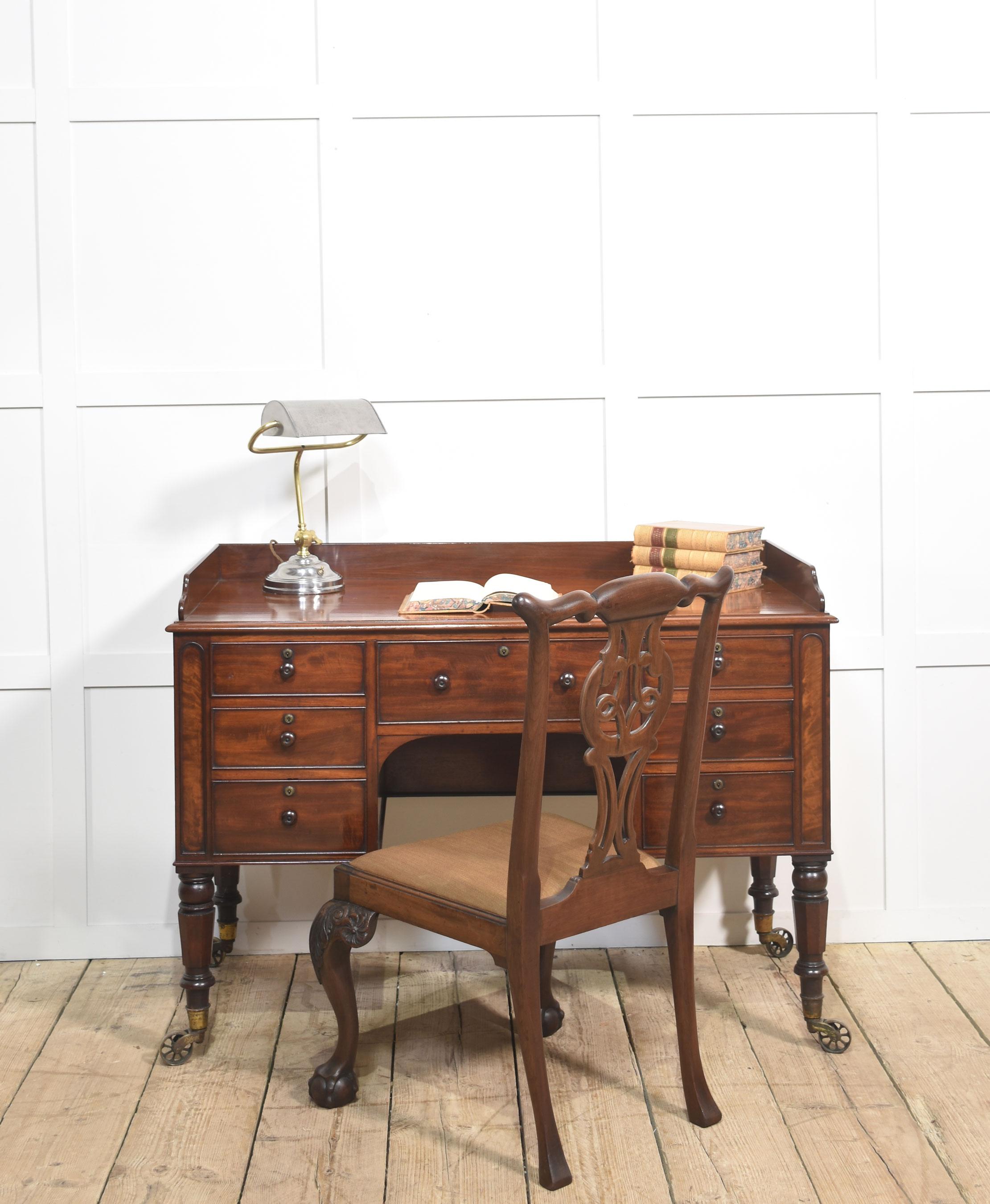 fine quality 19th century mahogany writing table, crafted with elegance and practicality in mind. The rectangular top features a raised gallery, ideal for keeping papers or accessories neatly in place. Below, a central drawer is flanked by two banks
