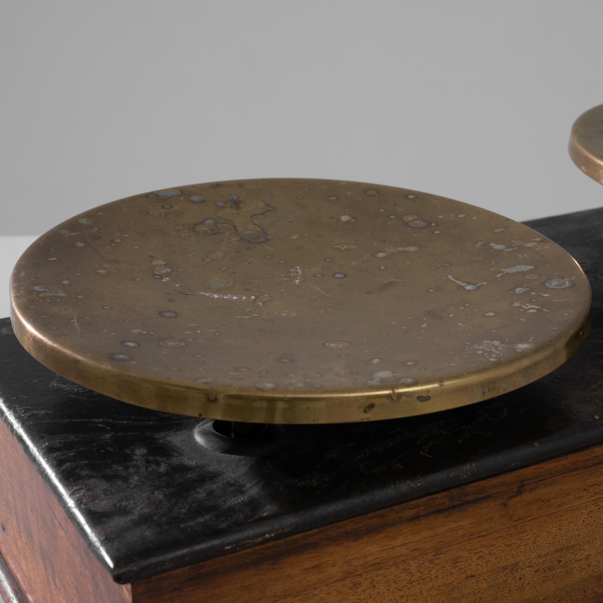 A 19th century metal and wooden scale produced in France, this piece embodies the savoir-faire of its manufacturer, Maison Béranger. A rectangular wooden case covered with a black metal top supports two oxidized copper trays showcasing delicate