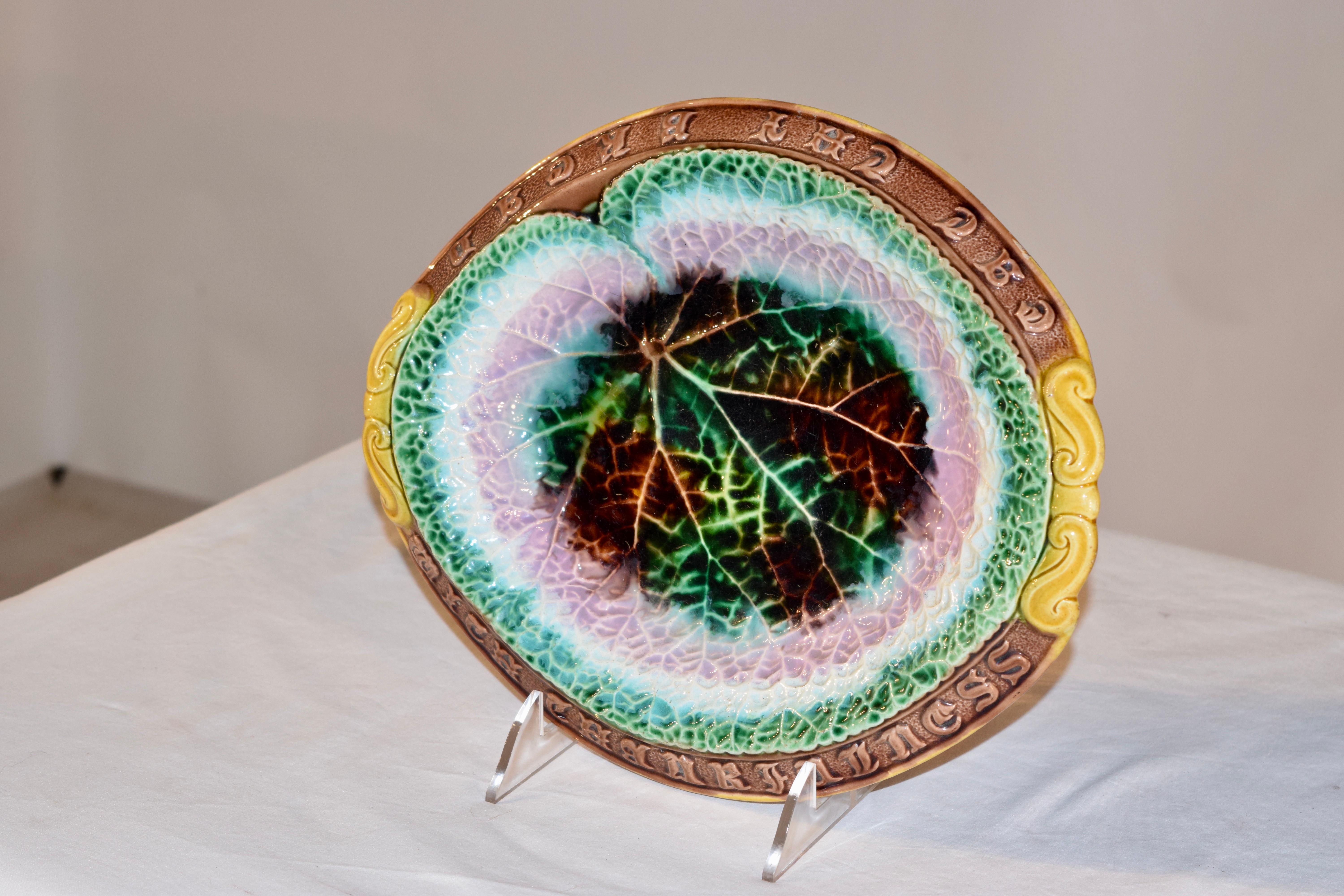 19th century Majolica bread tray in a lovely mold with a central leaf design in a multicolored palette of green, brown, pink and white, surrounded by a brown rim with gold accented handles and the words 