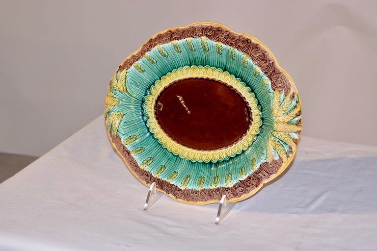 19th century Majolica bread tray from England in the wheat pattern. The tray has a central medallion of solid brown, surrounded by a yellow basket weave molding, with another surrounding edge of green and yellow wheat, and finished by a scalloped