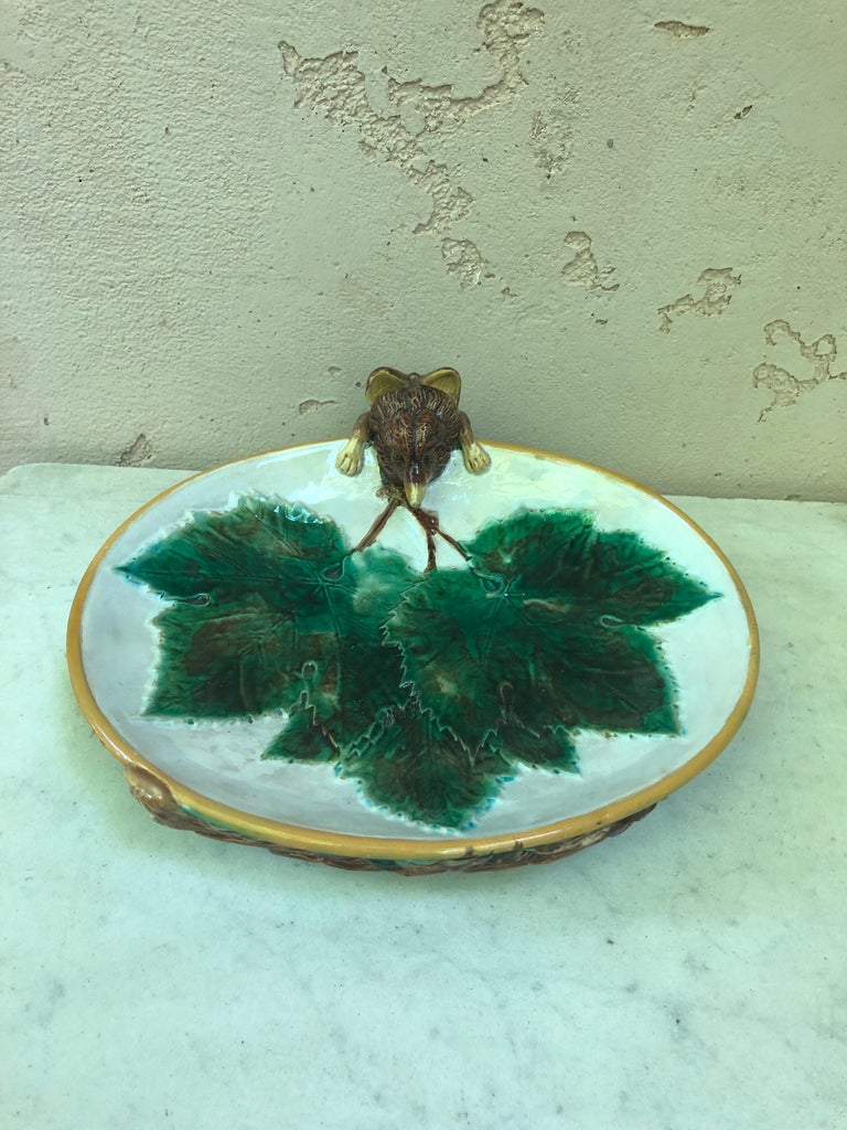 Majolica serving dish decorated with a three green vine leaves, the handle formed as a fox peering into the bowl with its tail appearing on the mottled underside signed George Jones.