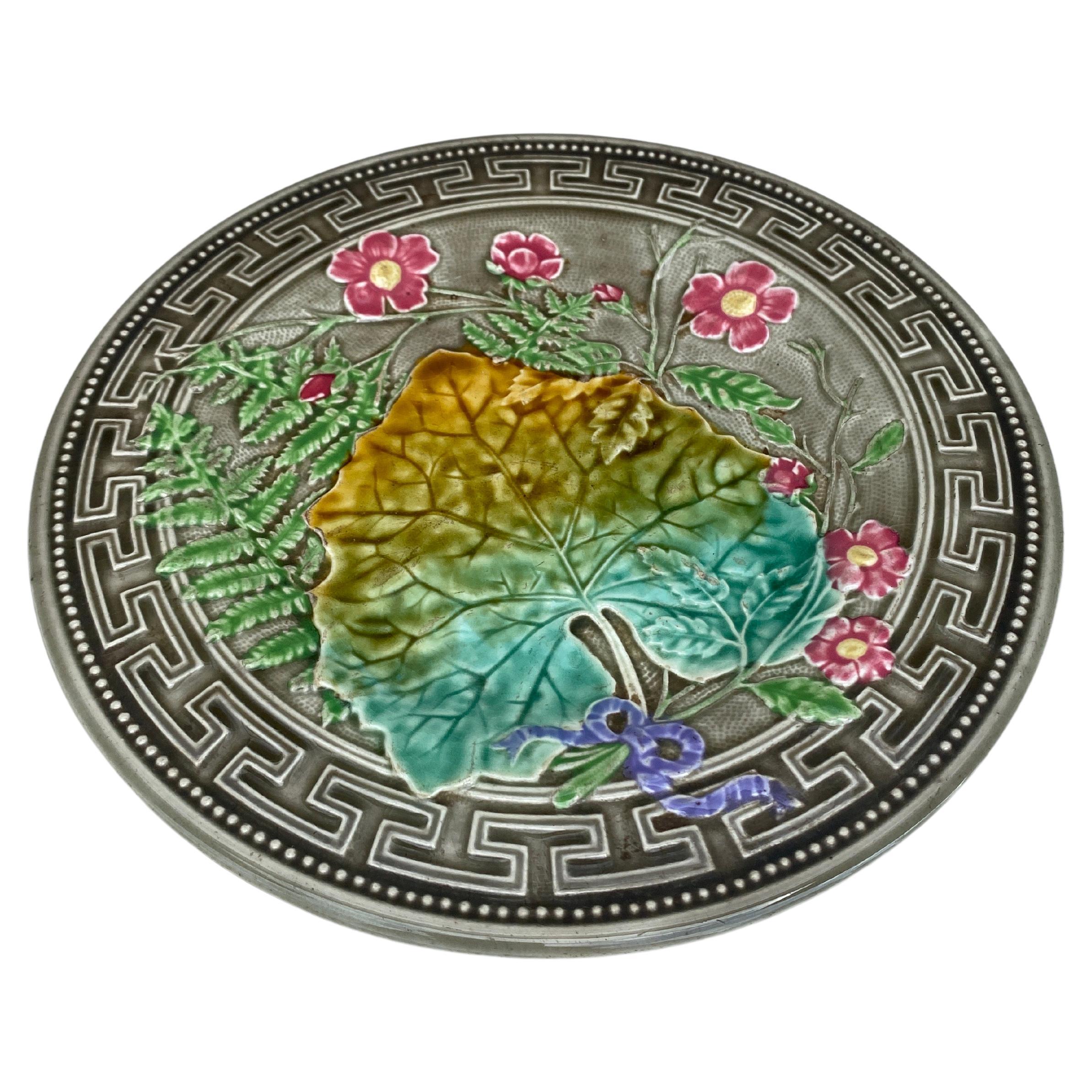 Plato de mayólica firmado Choisy le Roi, hacia 1890.
Decorada con hojas, helechos, flores rosas y cenefa griega.