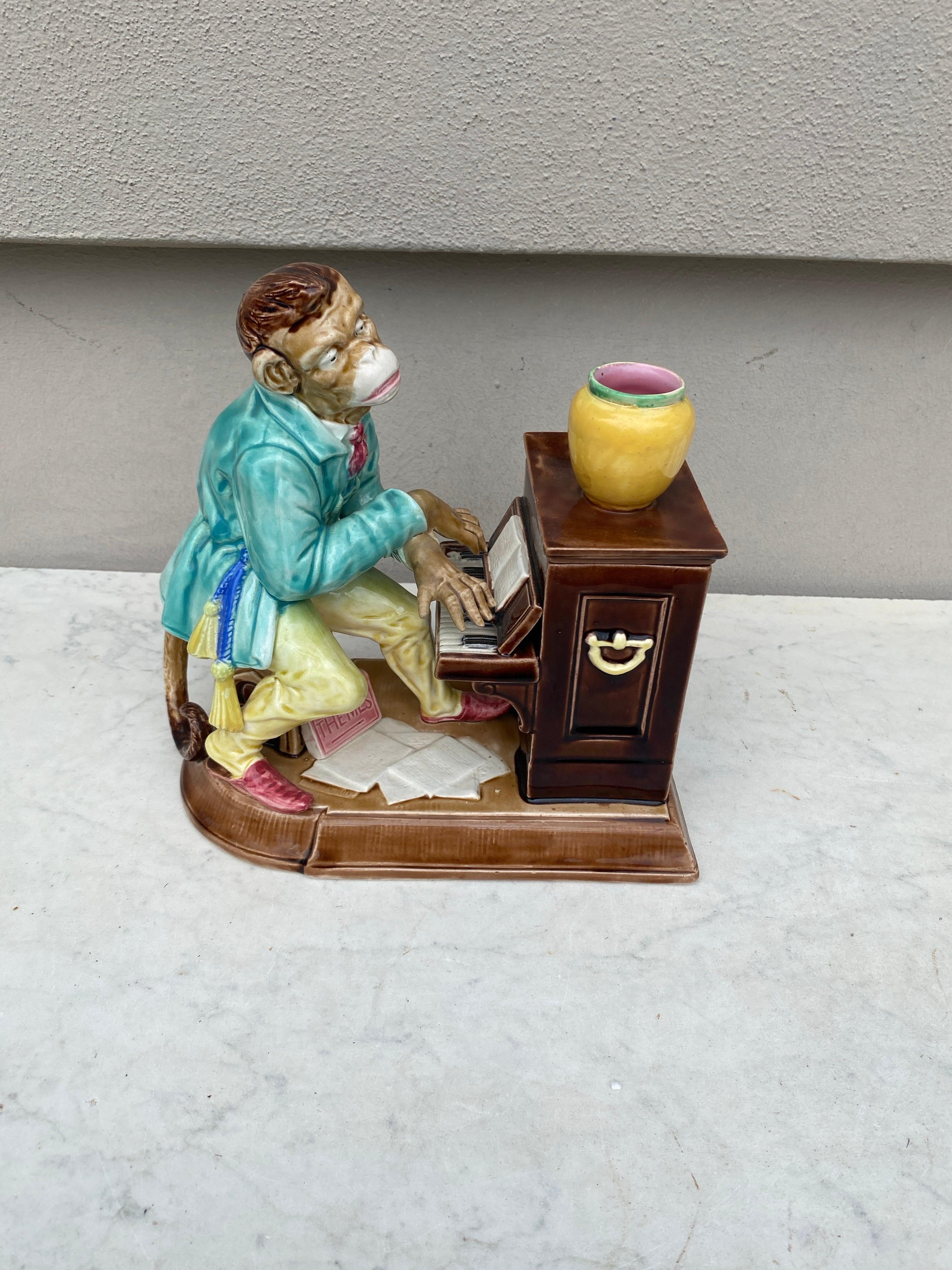 Amusant pot à tabac pour singe pianiste en majolique de Sarreguemines, vers 1880.Rarement trouvé complet avec son couvercle ,il porte un costume de style oriental, il joue du piano et deux livres sont représentés avec les titres
