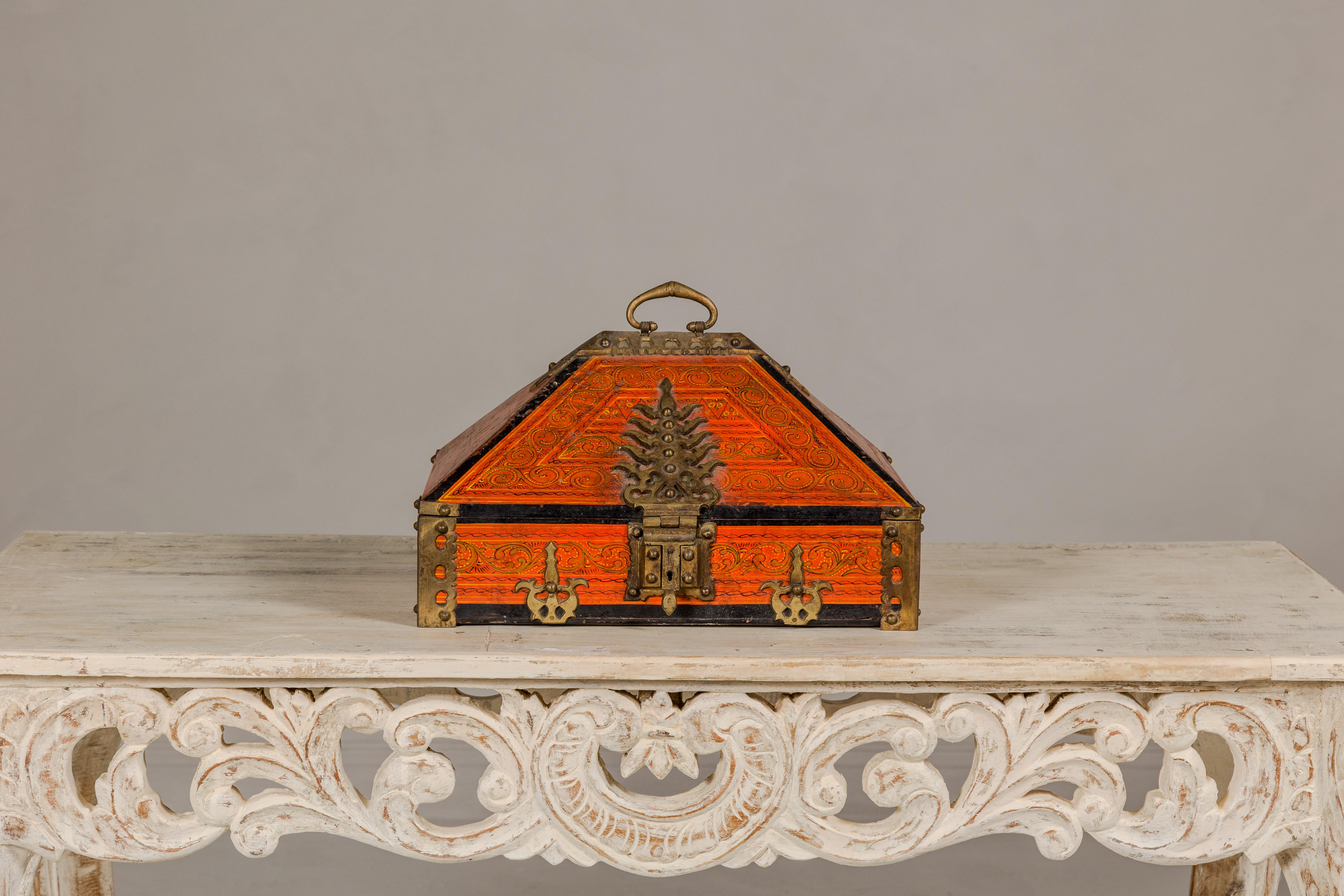 This South Indian jewelry box, known as a Malabar box, hailing from Kerala, is a magnificent piece of cultural artistry and historical significance. Its deep orange lacquer finish evokes the vibrant hues typical of the region, while the ornate brass