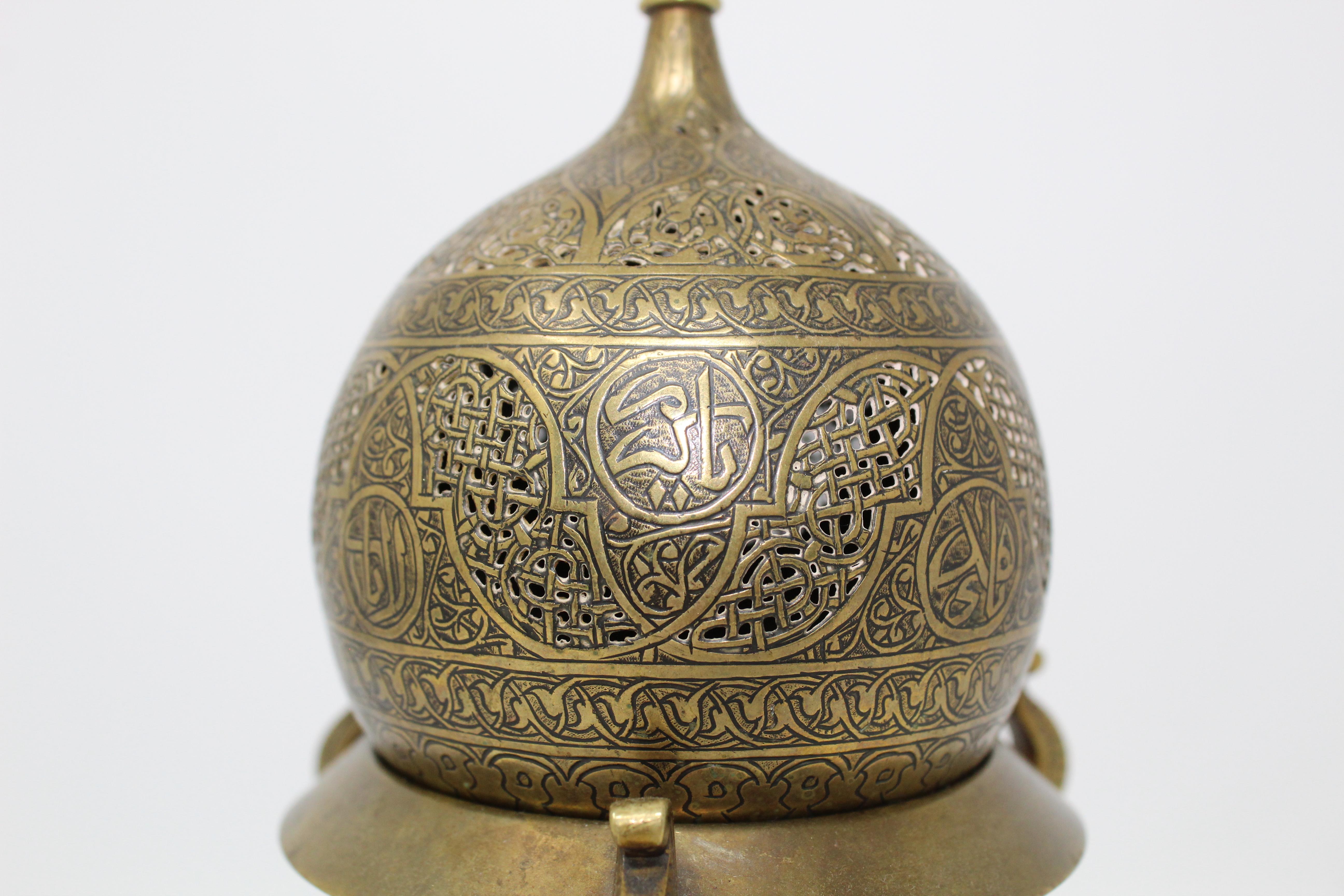 Resting on three feet, the tripod connected by three bars held by a sphere. Stylised vegetal motifs embellish the legs, where they meet the body of the censer, itself plain but for a silver inlaid band, engraved with an interlocking pattern. The