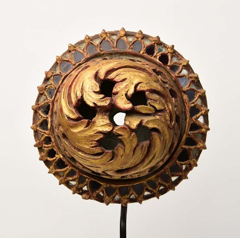 Burmese wood carving with gilded gold and glass.

Age: Burma, Mandalay Period, 19th Century
Size: Diameter 21.8 C.M. / Thickness 11.5 C.M.
Size including stand: Height 58 C.M.
Condition: Nice condition overall (some expected degradation due to its