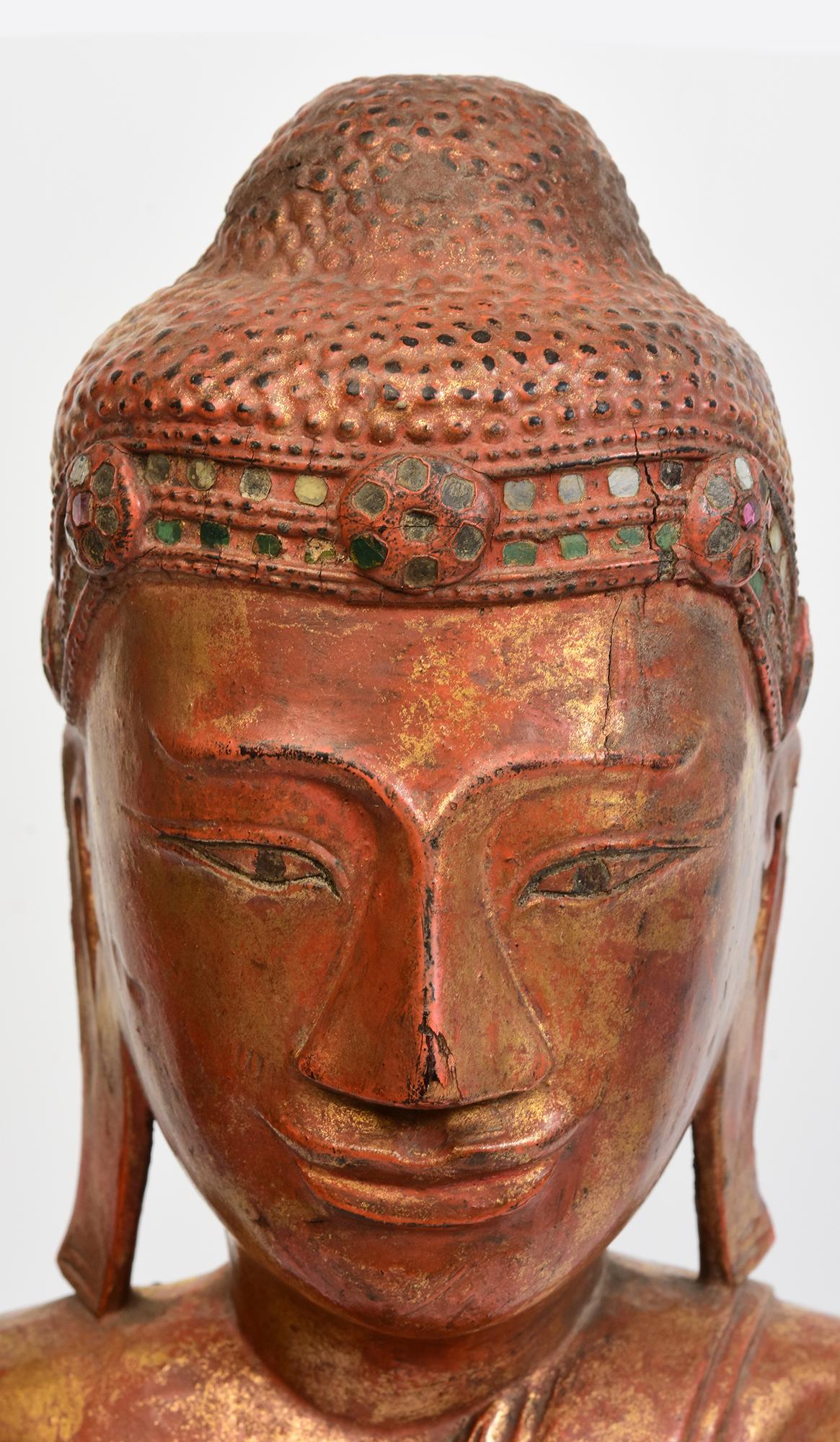 Bouddha ancien en bois birman assis en posture Mara Vijaya (appelant la terre à témoin) sur une base, avec laque, or doré et incrustation de pièces de verre colorées sur le bandeau.

Âge : Birmanie, période Mandalay, 19e siècle
Taille du Bouddha
