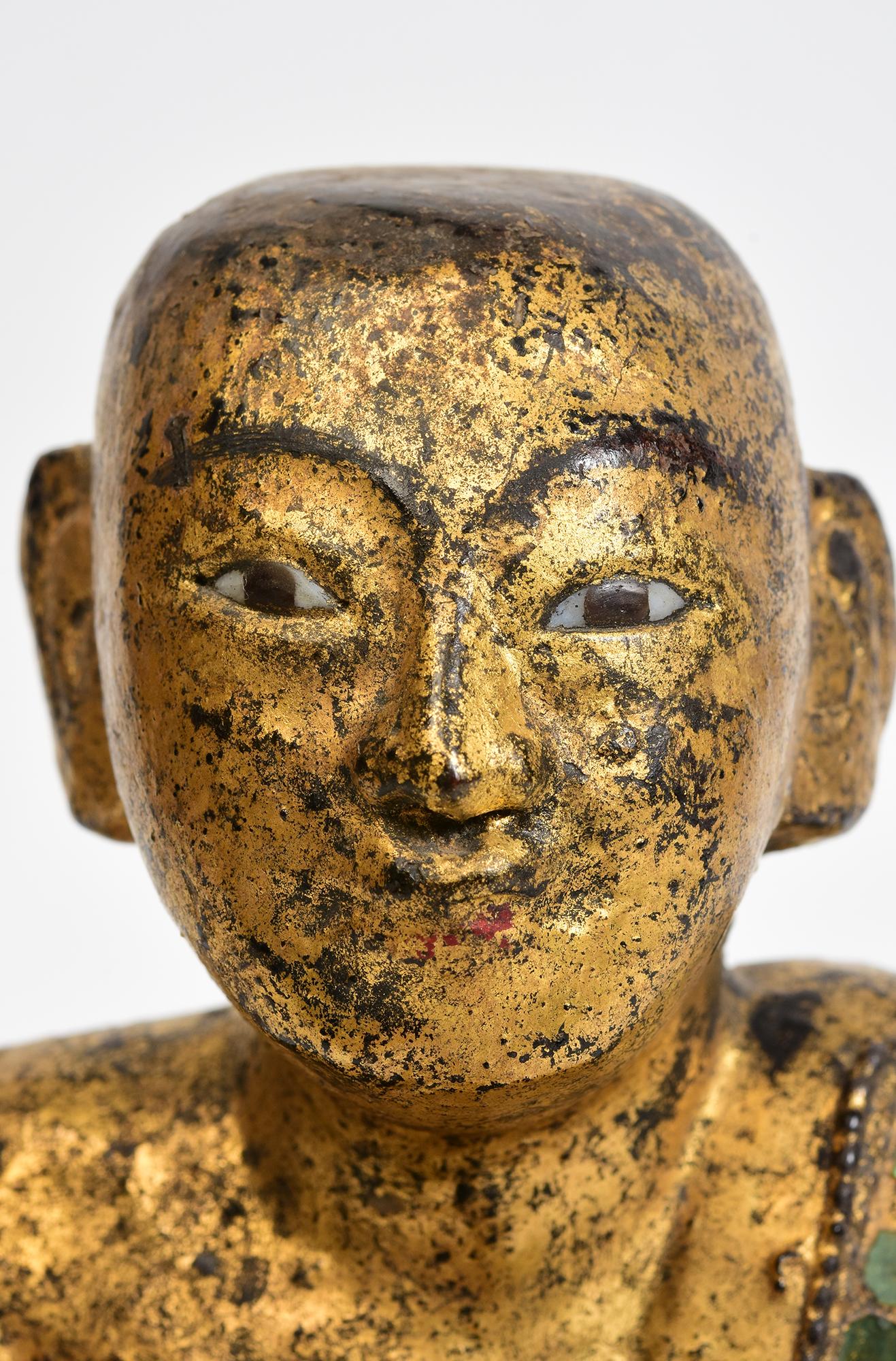 Antique Burmese wooden seated disciple, with gilded gold and inlay of colorful glass pieces on the borders of the robes.

Age: Burma, Mandalay Period, 19th Century
Size: Height 20.3 C.M. / Width 16.5 C.M. / Length 15.7 C.M.
Condition: Nice condition