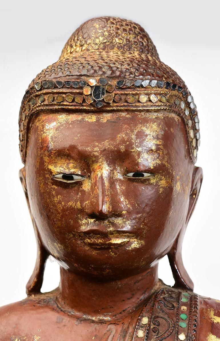 Burmese wooden Buddha standing on a base, with lacquer and inlay of colorful glass pieces on the headband and borders of the robe.

Age: Burma, Mandalay Period, 19th century
Size: Height 79.3 C.M. / Width 40.4 C.M.
Size including stand: Height