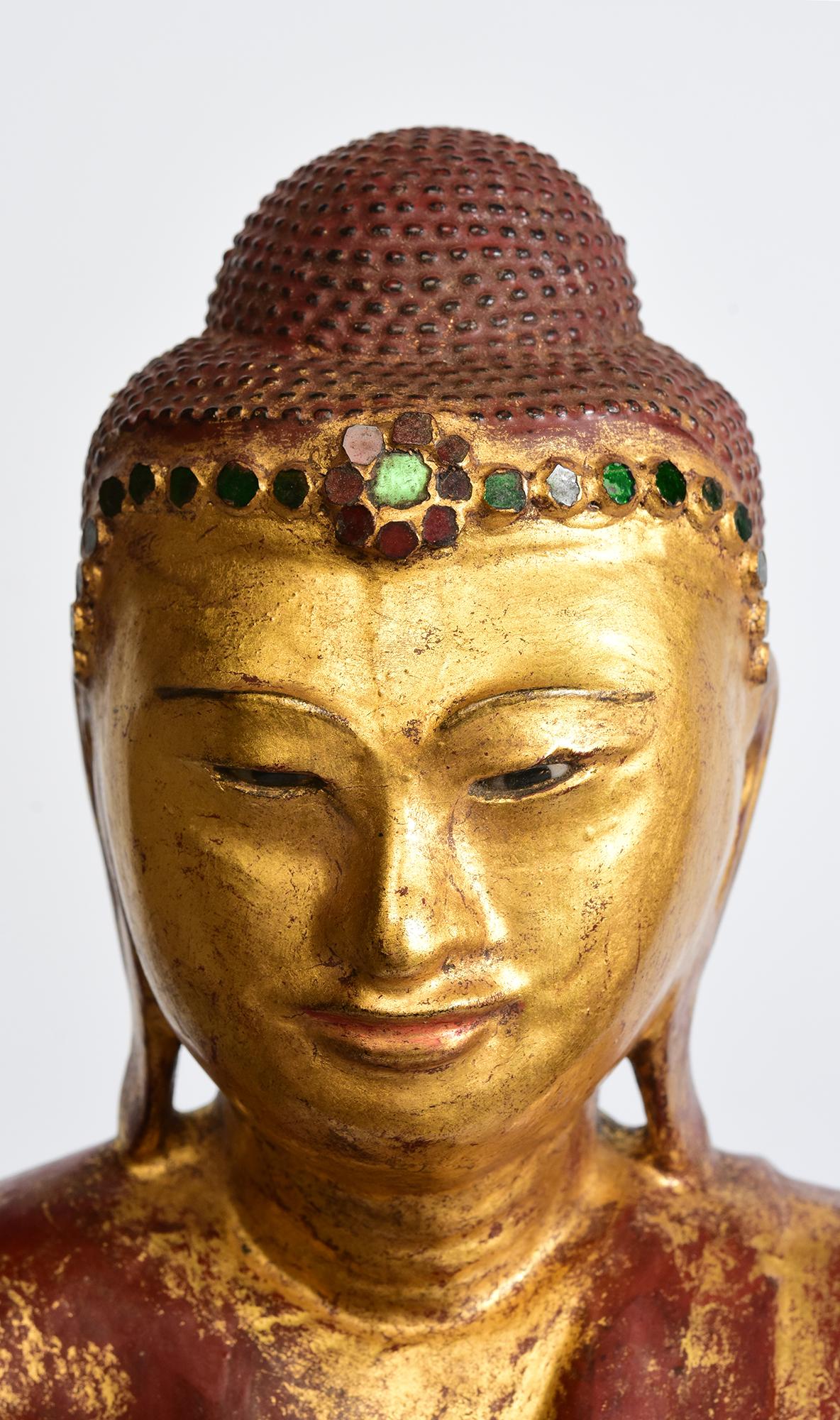 Antique Burmese wooden Buddha standing on a lotus base, with gilded gold and inlay of colorful glass pieces on the headband.

Age: Burma, Mandalay Period, 19th Century
Size: Height 52.2 C.M. / Width 25.3 C.M.
Height including stand: 71.2