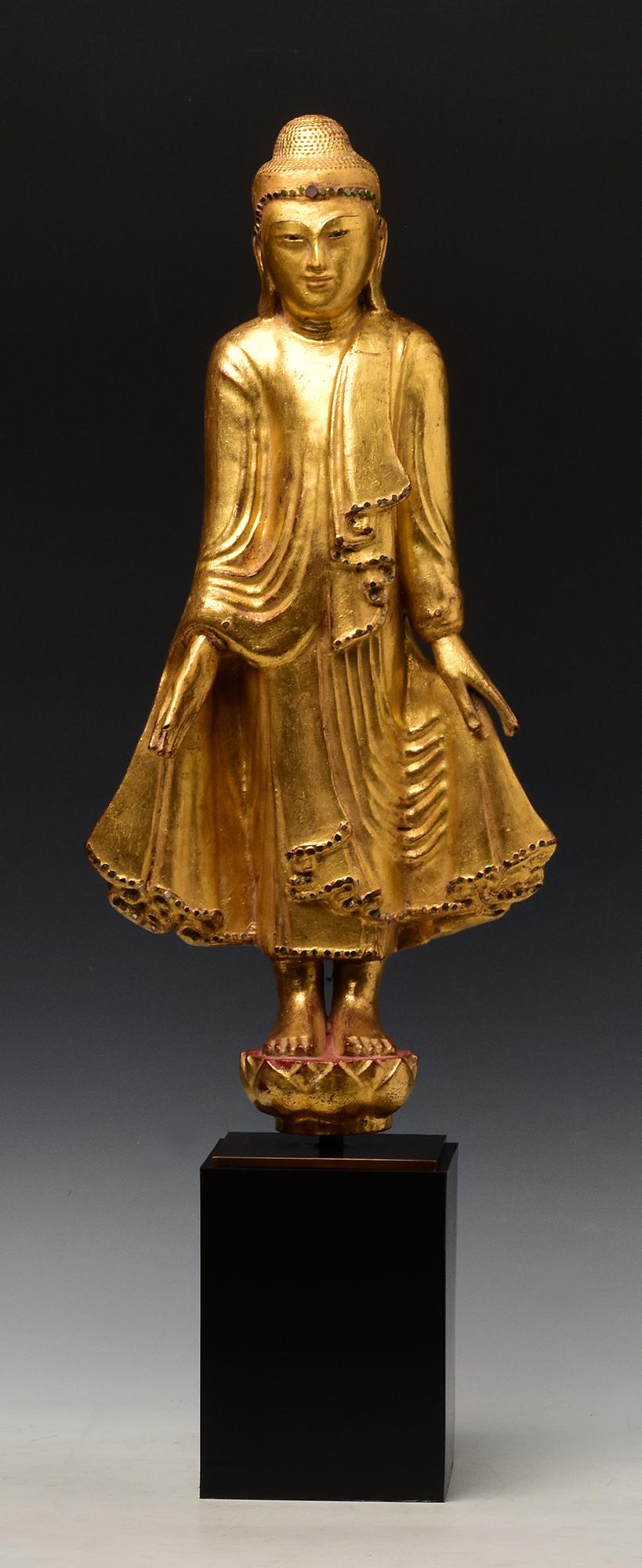 Antique Burmese wooden Buddha standing on a lotus base, with gilded gold and inlay of colorful glass pieces on the headband and the borders of the robe.

Age: Burma, Mandalay Period, 19th Century
Size: Height 54 C.M. / Width 25.5 C.M.
Height