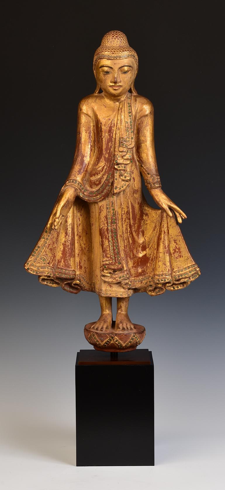 Antique Burmese wooden Buddha standing on a lotus base, with gilded gold and inlay of colorful glass pieces on the headband and borders of the robe.

Age: Burma, Mandalay Period, 19th Century
Size of Buddha only: Height 54.5 C.M. / Width 29.9