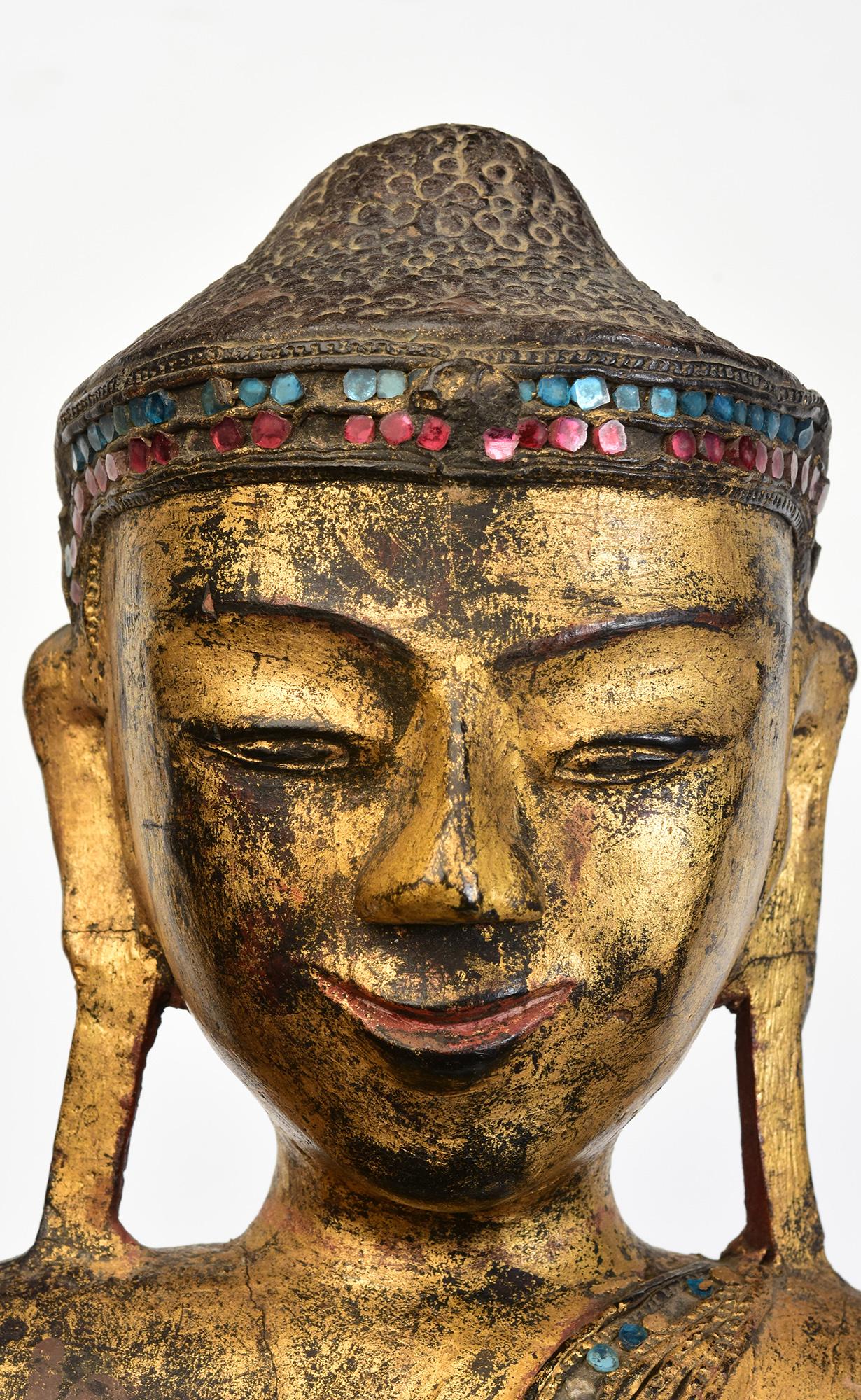 Antiker burmesischer stehender Buddha aus Holz, mit lackiertem, vergoldetem Gold und Intarsien aus bunten Glasstücken auf dem Stirnband und den Rändern des Gewandes.

Alter: Birma, Mandalay-Periode, 19. Jahrhundert
Größe des Buddhas allein: Höhe