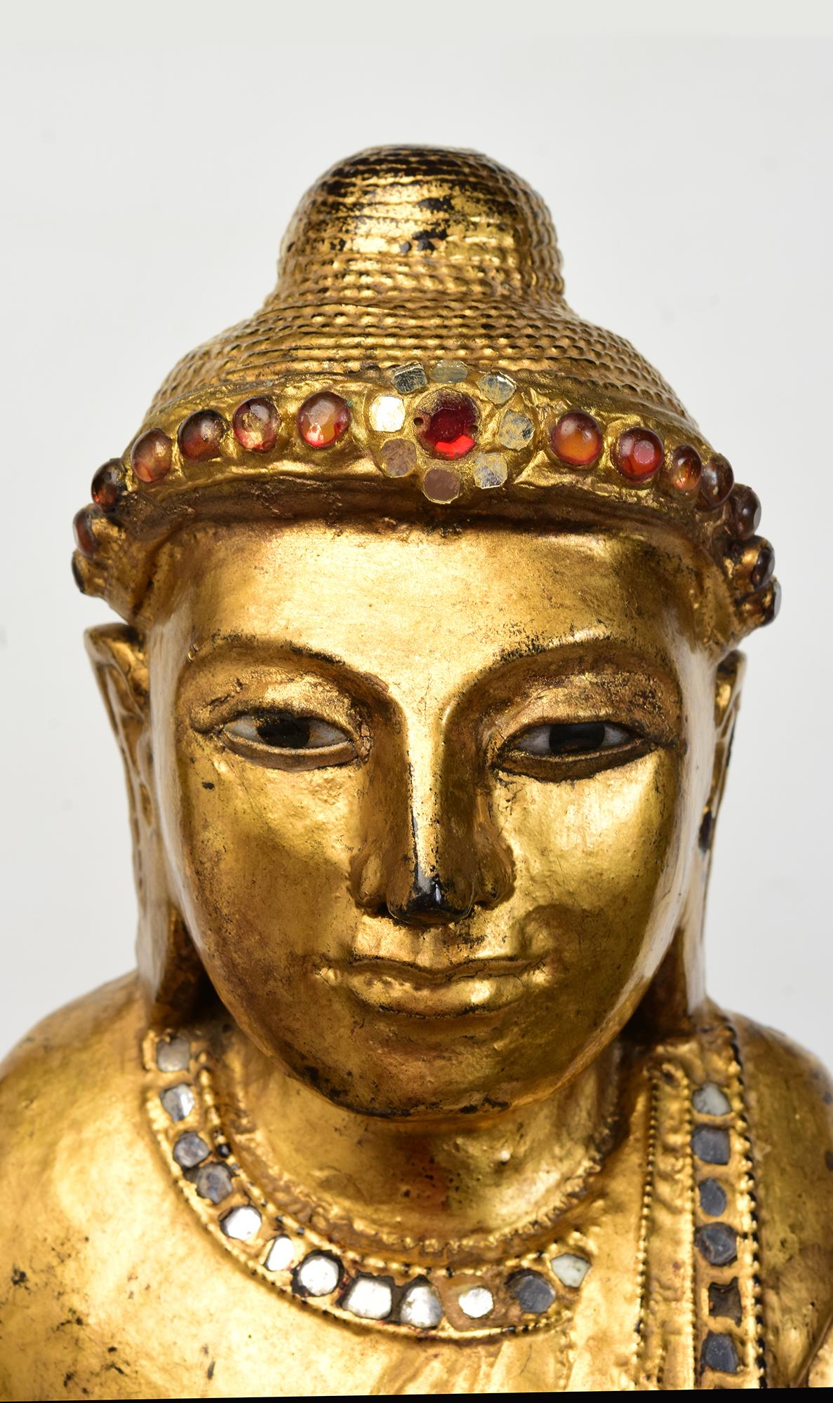 Antique Burmese wooden Buddha standing on a lotus base, with gilded gold and inlay of colorful glass pieces on the headband and borders of the robe.

Age: Burma, Mandalay Period, 19th Century
Size excluding black stand: Height 68 C.M. / Width 32