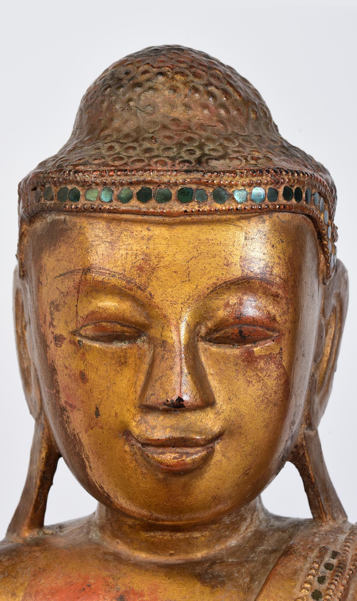 Antico Buddha birmano in legno che poggia su una base di loto, con oro dorato e intarsi di pezzi di vetro colorati sulla fascia e sui bordi della veste.

Età: Birmania, Periodo Mandalay, XIX secolo
Dimensioni, escluso il supporto nero: Altezza 65,2