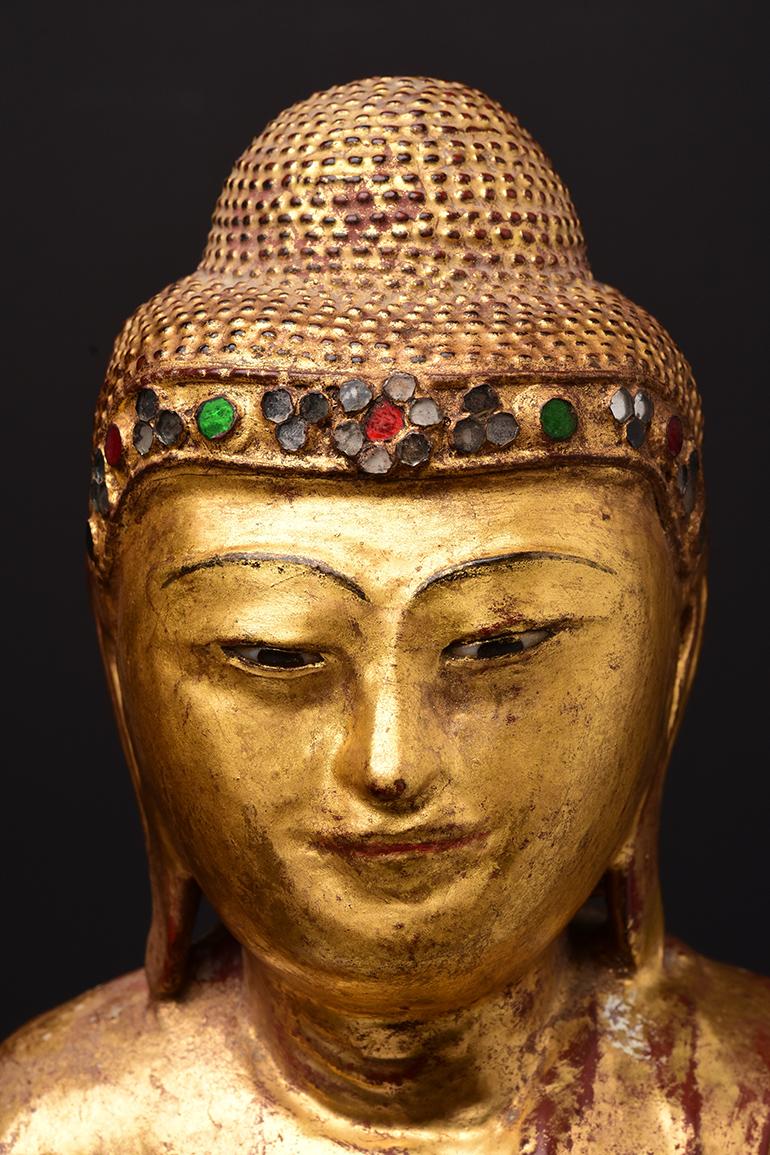 Antiker burmesischer Holzbuddha auf einem Lotussockel, vergoldet und mit bunten Glasstücken am Stirnband versehen.

Alter: Birma, Mandalay-Periode, 19. Jahrhundert
Größe: Höhe 53,6 C.M. / Breite 25,5 C.M.
Höhe mit Ständer: 72.3 C.M.
Zustand: