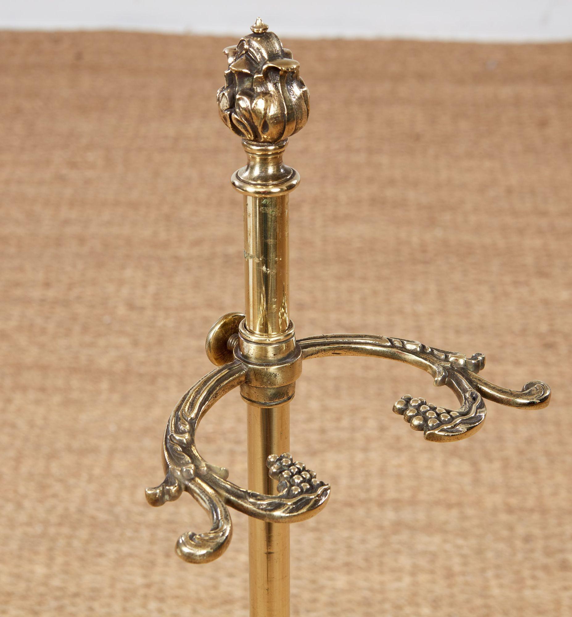A brass and white marble umbrella stand with elegant tall brass shaft topped with cast foliate finial, an adjustable holder with vine cast arms, mounted on a thick marble block carved with drip lines and four dished drip-collector divots.  Also