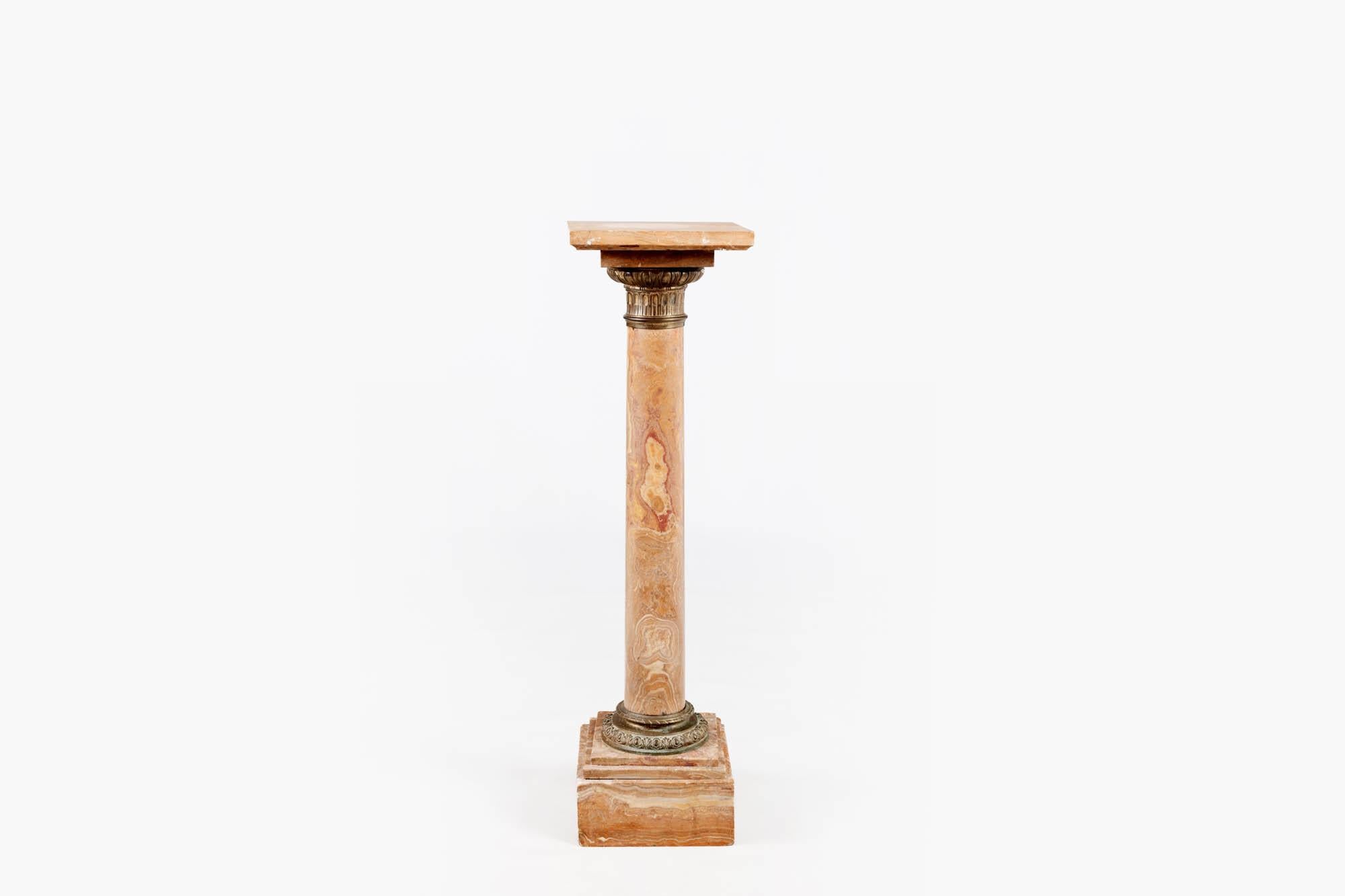Basamento in marmo del XIX secolo con montature in ottone a forma di colonna classica. Il solido fusto cilindrico, in marmo beige, bianco e ocra, poggia su una base quadrata. La colonna è circondata da uno spesso anello di bronzo con dettagli