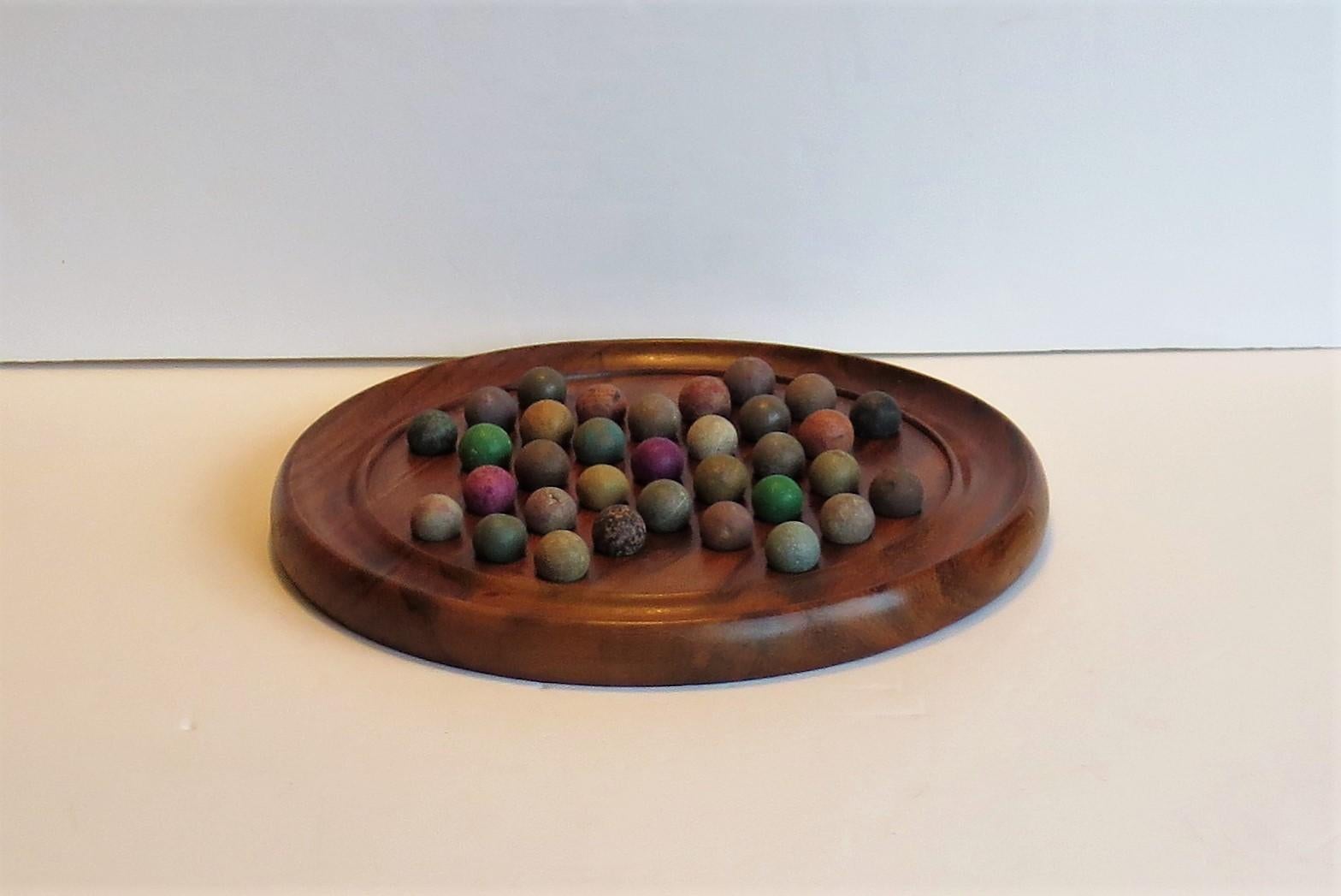 This is a complete game of marble solitaire, having a very good walnut board and a complete set of early clay and stone 19th century marbles.

The circular turned board is made of walnut and has an excellent natural grain pattern and color. The