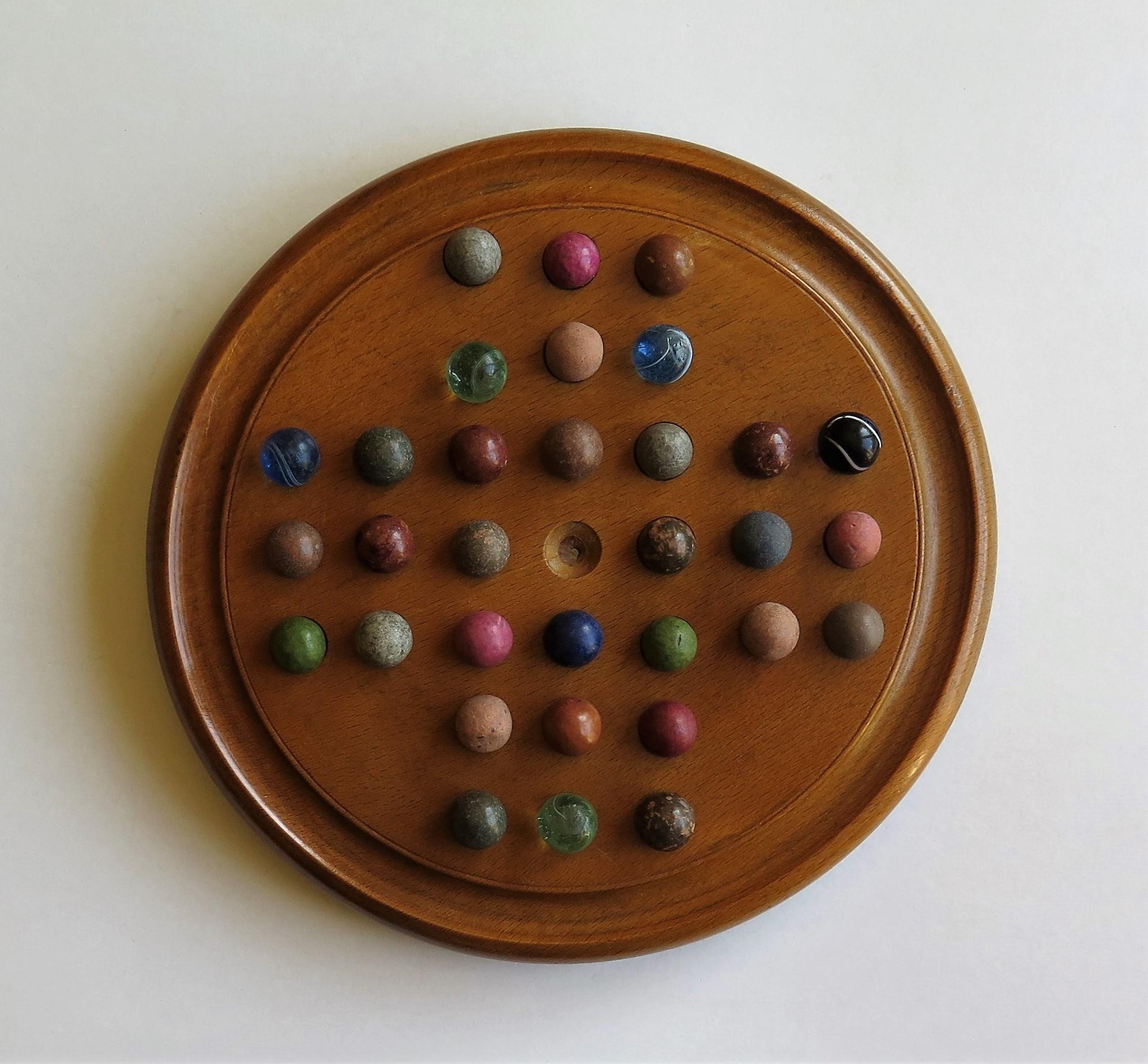 This is a complete game of marble solitaire from the late 19th century with 32 early handmade marbles.

The circular turned board is made of beech or ash and sits on three small wooden bun feet secured with wood screws. The board has 32 holes with