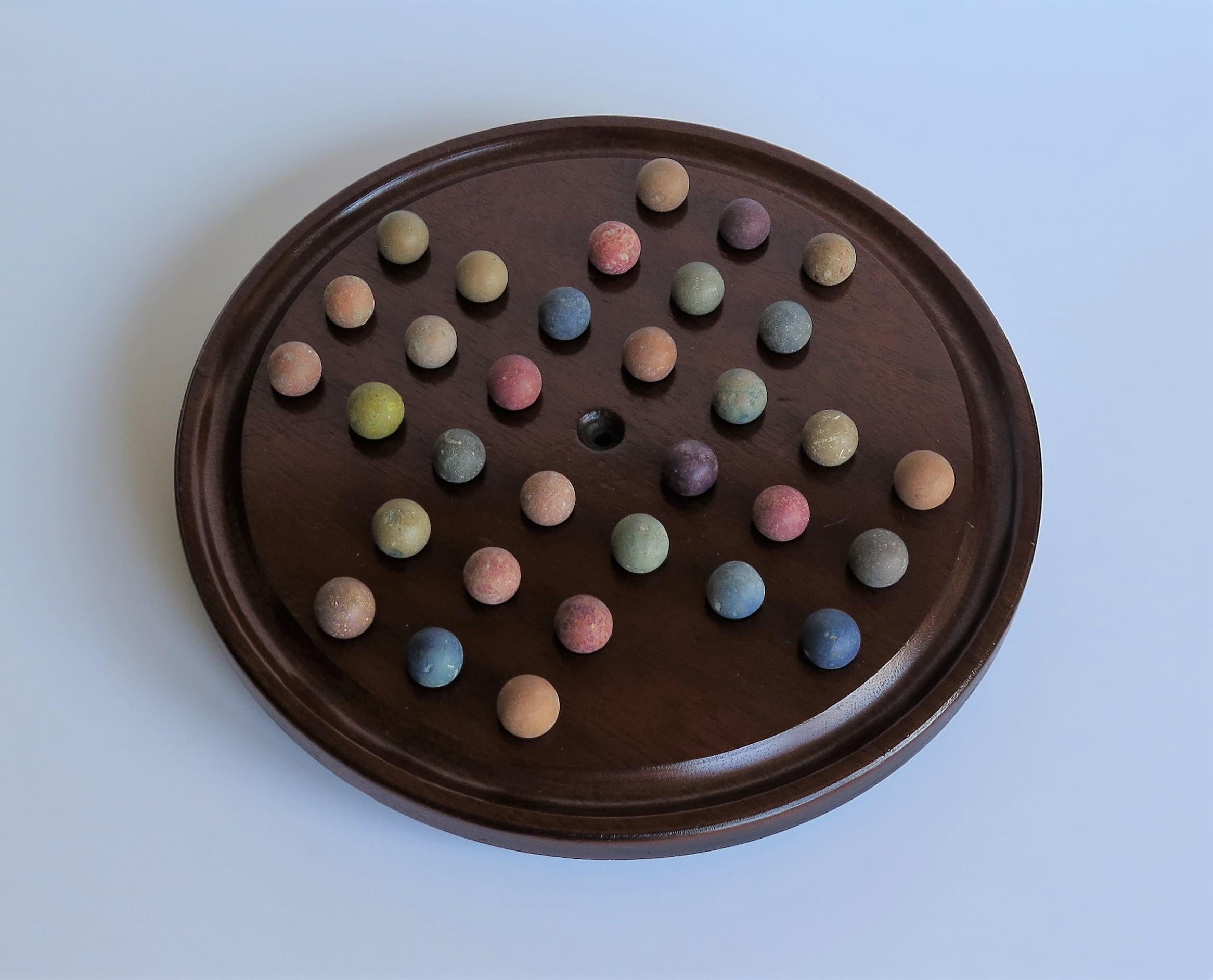 This is a complete Victorian board game of marble solitaire, with a lovely hand turned mahogany board and 32 early ceramic clay and stone hand made marbles, all dating to the 19th century. 

The circular board has a larger than normal diameter of