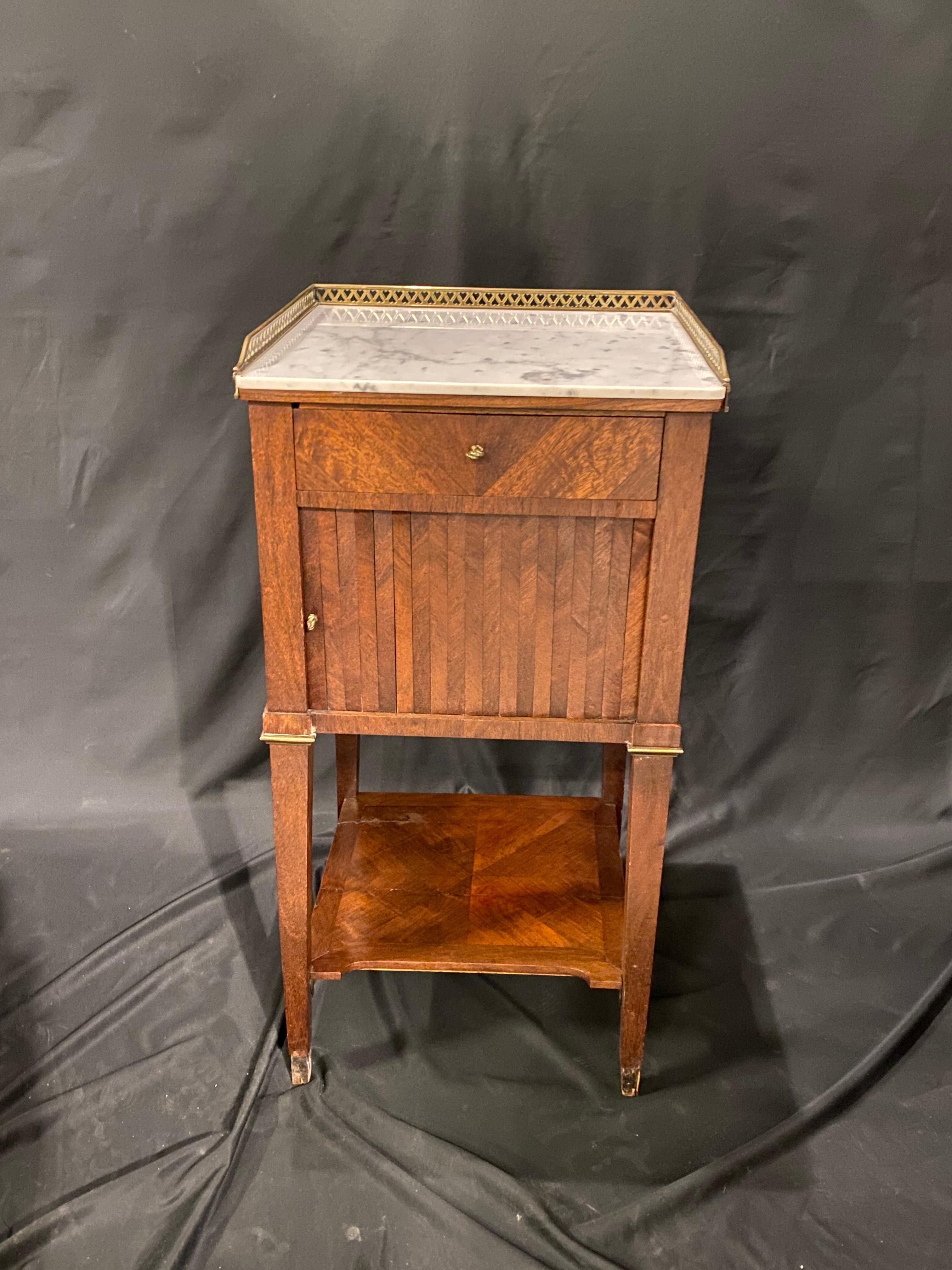 This 19th century French walnut side table with a lovely patina developed with age. The off white marble top is framed on three side with a brass gallery. The table has one drawer and a tambour door below, with a shelf at the base of the legs.