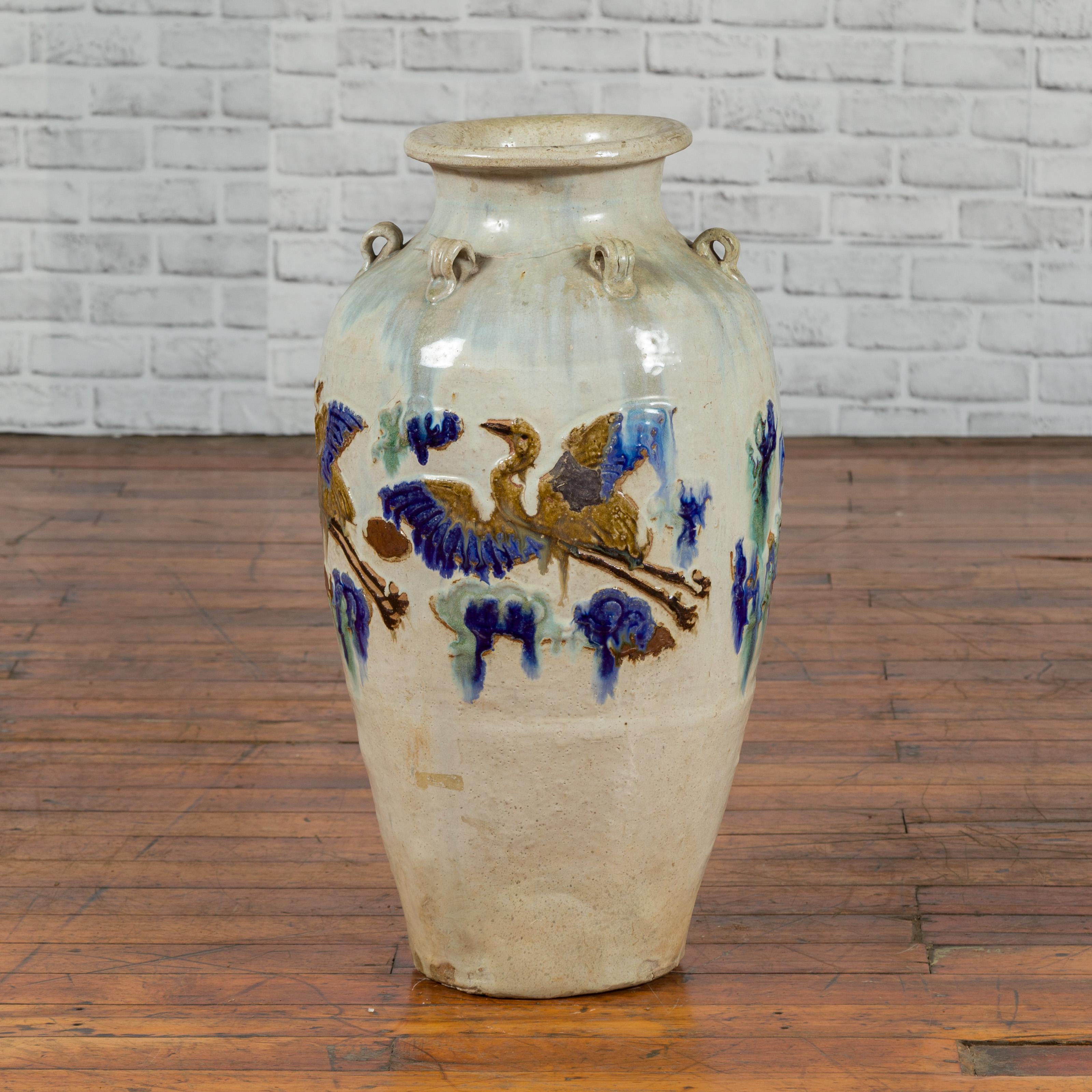 A Martaban vase from the 19th century, with white, blue and green motifs. Created during the 19th century, this Martaban vase is adorned with a series of petite loop handles through which a rope would have been passed to secure a top. The belly