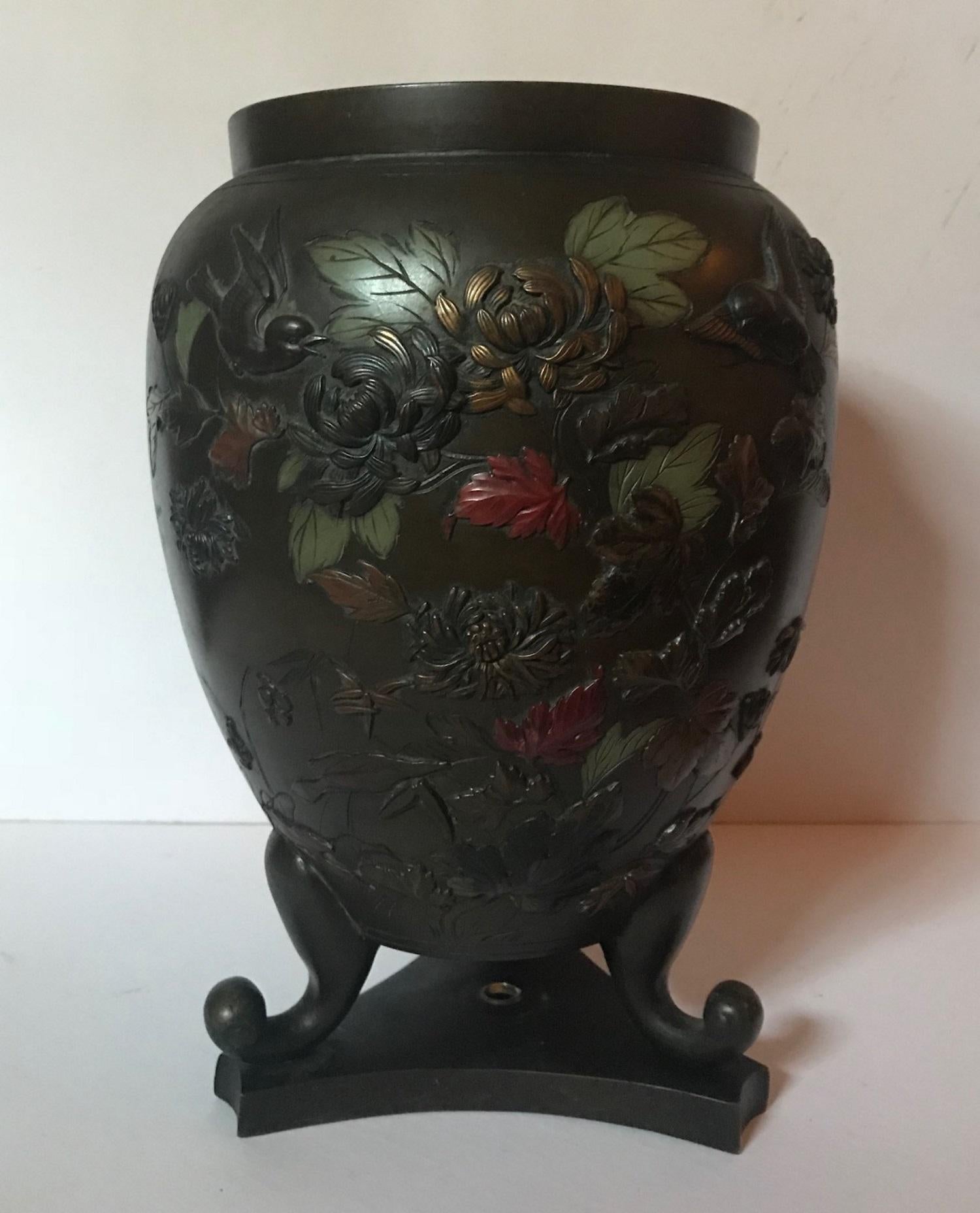 This beautiful baluster shaped bronze vase has a rich dark patina. The entire body is adorned with abundant foliage, blossoms and swallows in relief casting. Every flower is highlighted in muted colors with gilt accents. The vase sits on three