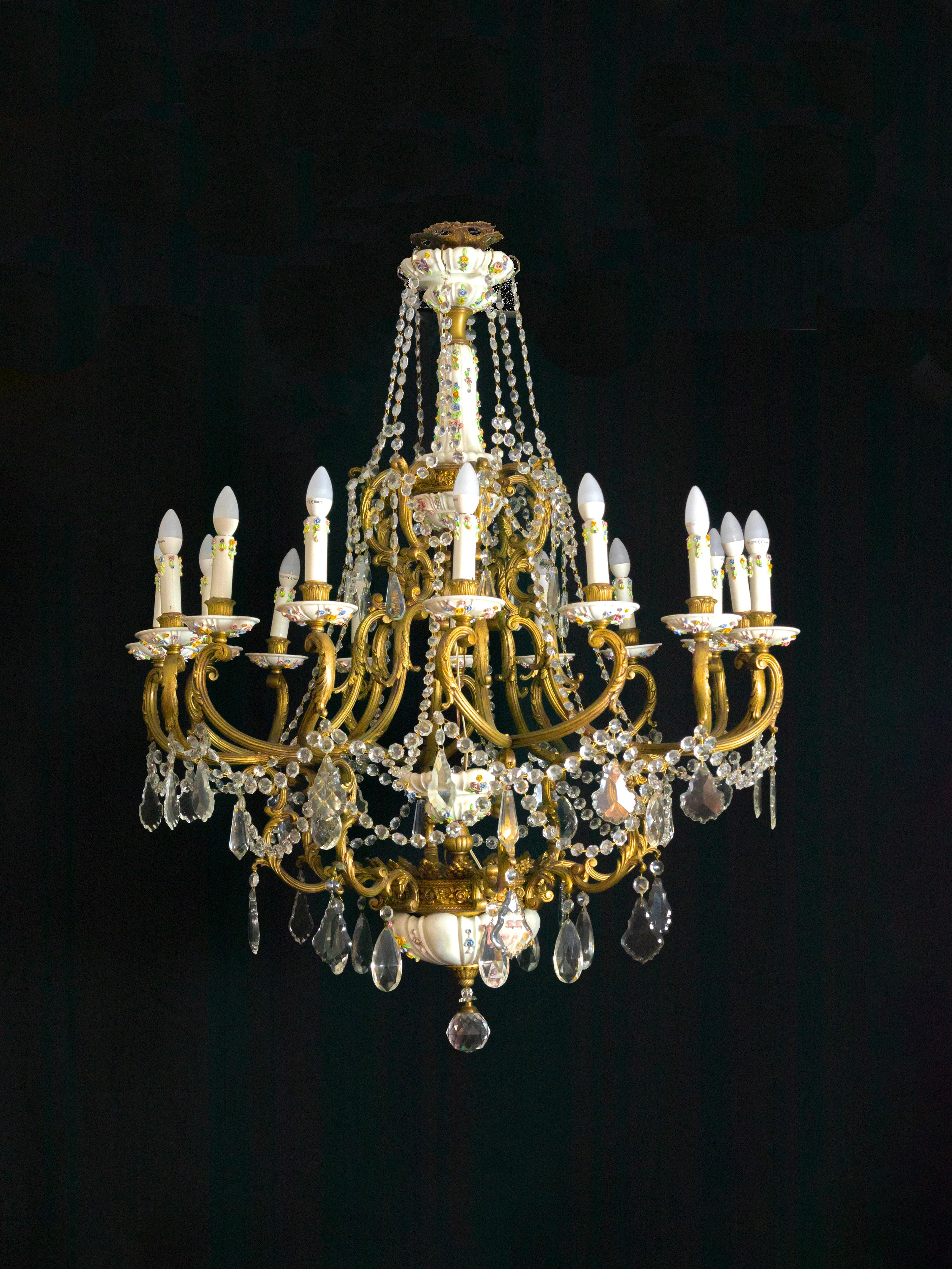 A large 19th-century chandelier featuring sixteen gilt bronze arms and hand-painted floral and vegetal motifs. The structure is adorned with Maissen porcelain elements and richly decorated with hanging glass pendants.

The delicately enameled