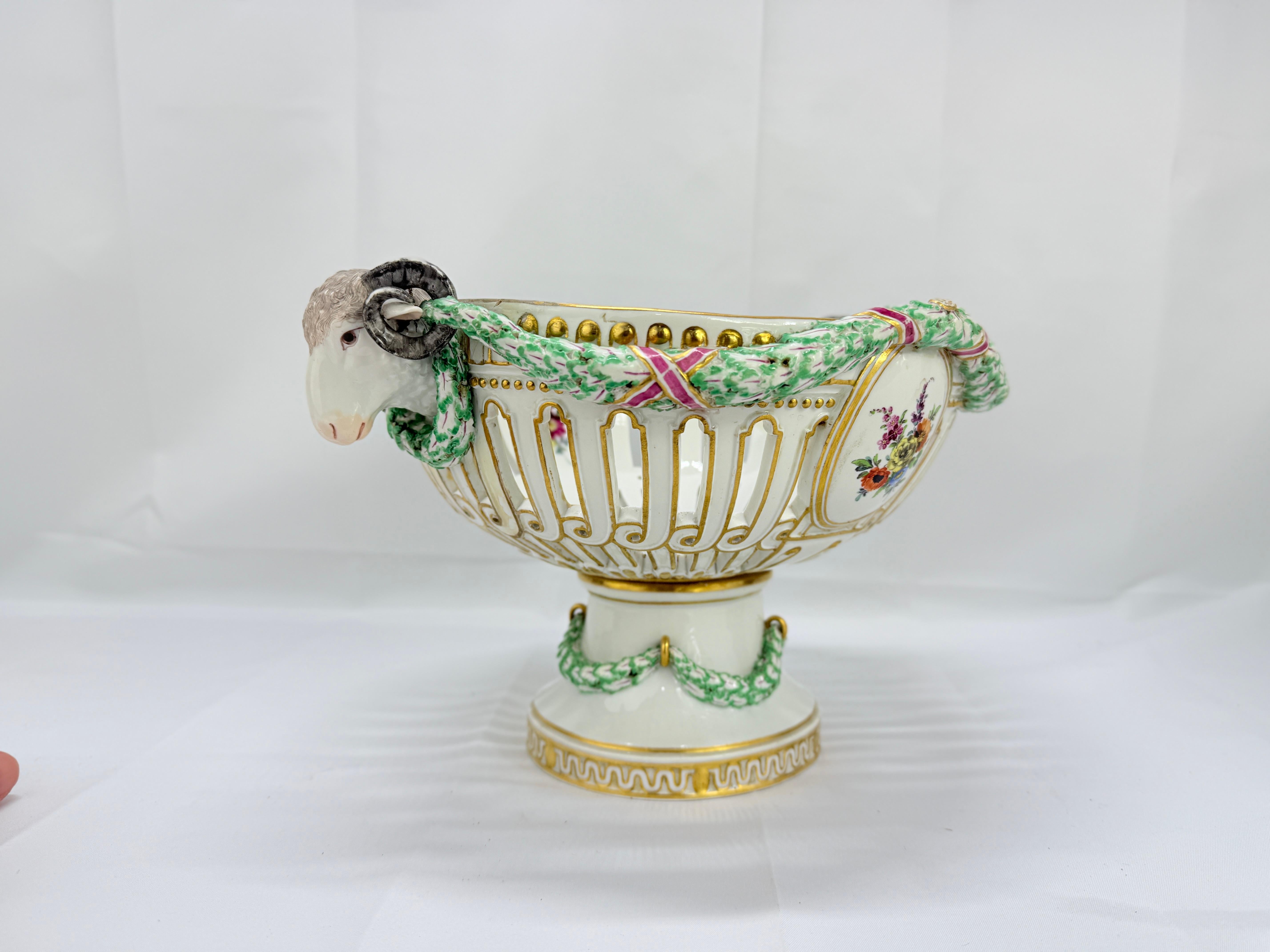A Meissen porcelain centerpiece of oval openwork construction, two floral windows oppose each of the main bodies of the piece and are flanked by a pair of beautiful ram's head handles connected with green laurel festoons and purple x loops. The