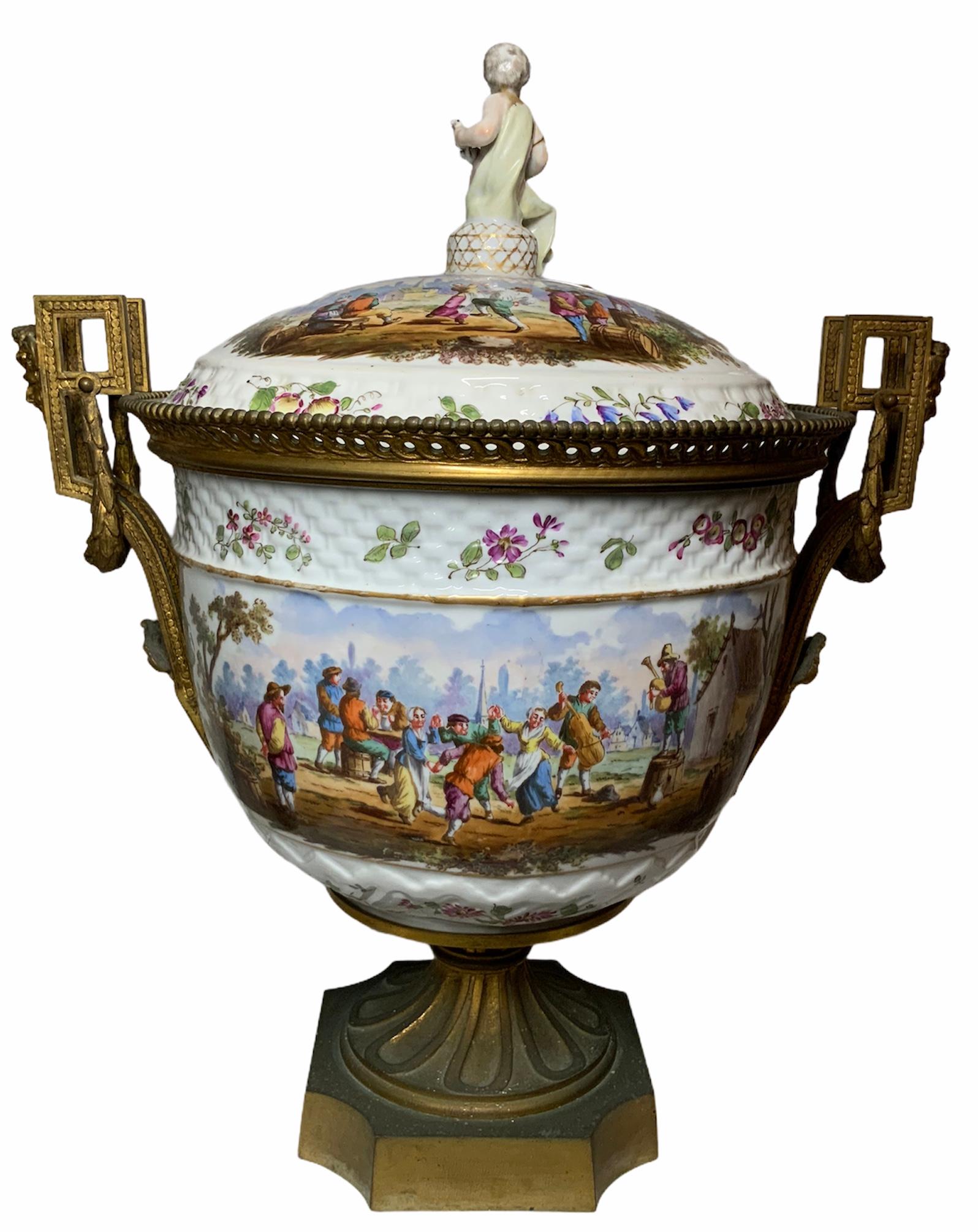 This is a gilt bronze mounted and hand painted porcelain large bowl vase with lid. The hand painted continuous scene shows a town celebration with some peasants dancing & playing some instruments while others are drinking. Around the top & bottom