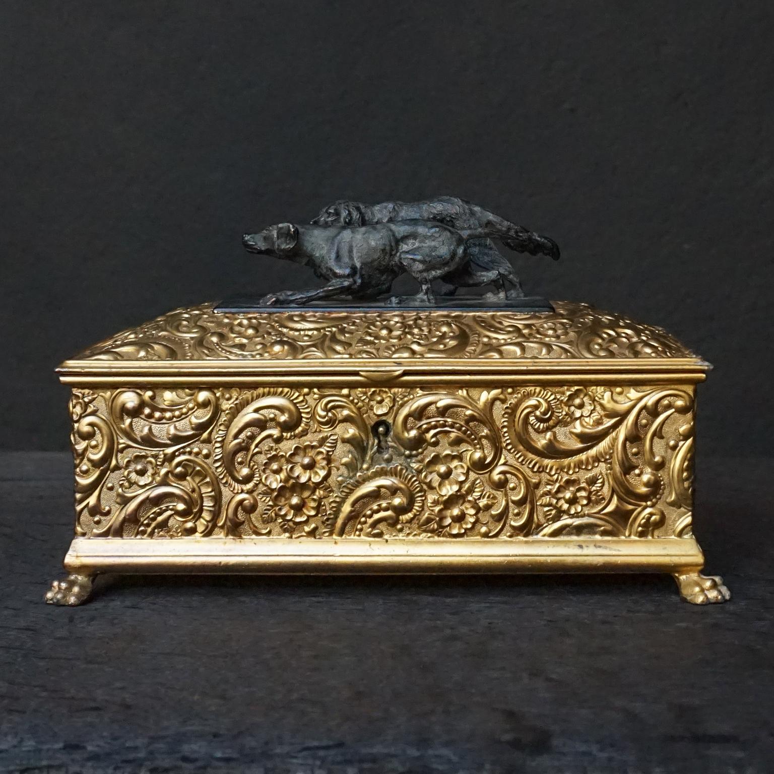 Highly detailed quadruple plated silver cigar humidor, with repoussé floral motif.
Rectangular heavy box with two figural hunting dogs in bronze on the hinged lid. 
Inside two compartments separated by a small middle compartment.

Made by Wilcox