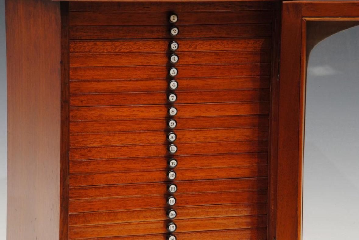 Une belle boîte à glissière en acajou du 19e siècle avec une porte vitrée et une poignée de transport en laiton d'origine, contenant 20 tiroirs, chacun avec des boutons d'ébène numérotés. Tous avec 14 diapositives.

vers 1845.
