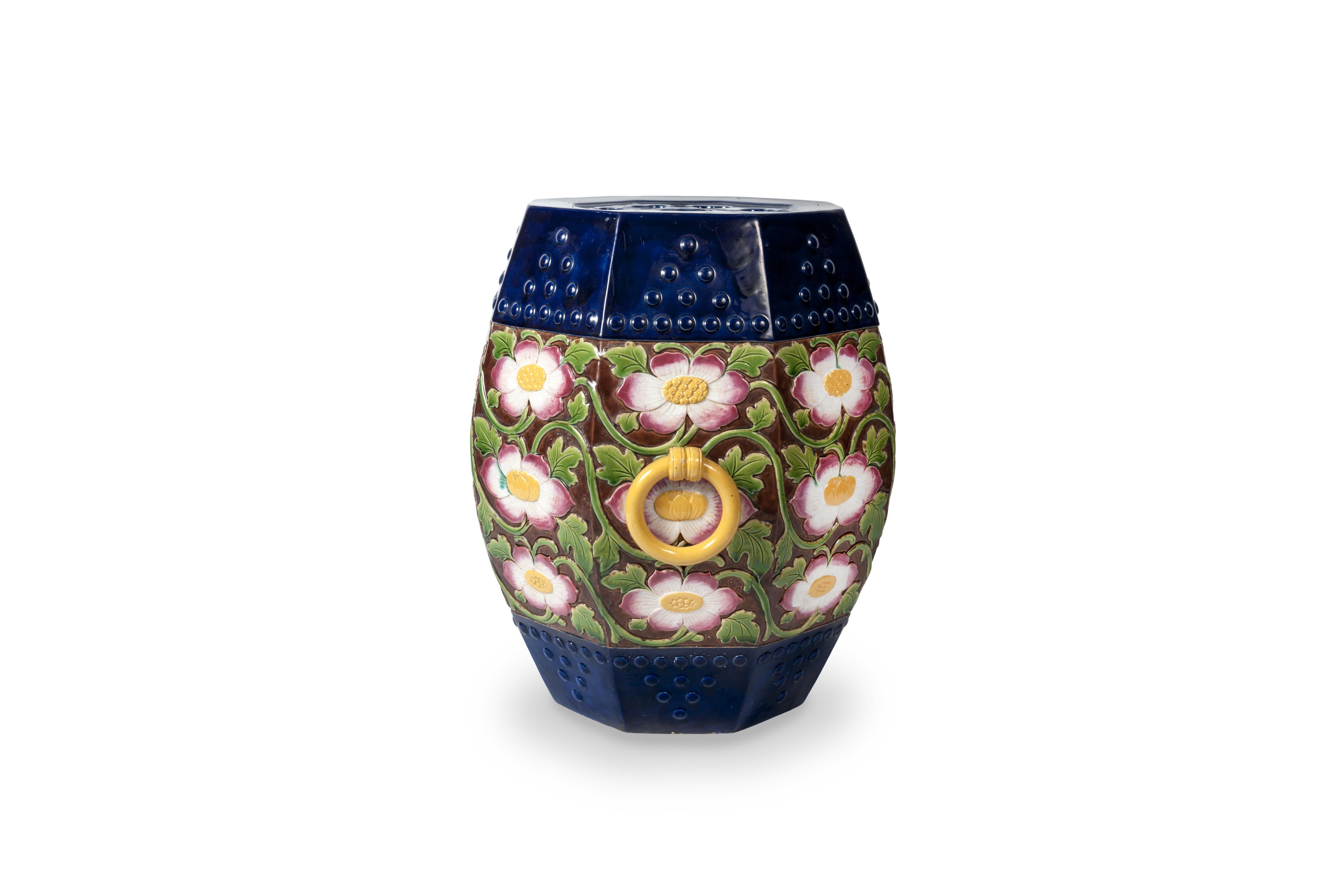 This superb garden seat or garden stool is the work of the British manufacturer Minton. Its original shape of a faceted drum receives a floral decoration on a brown background. The large flowers, bursting with golden buds, reveal white petals with