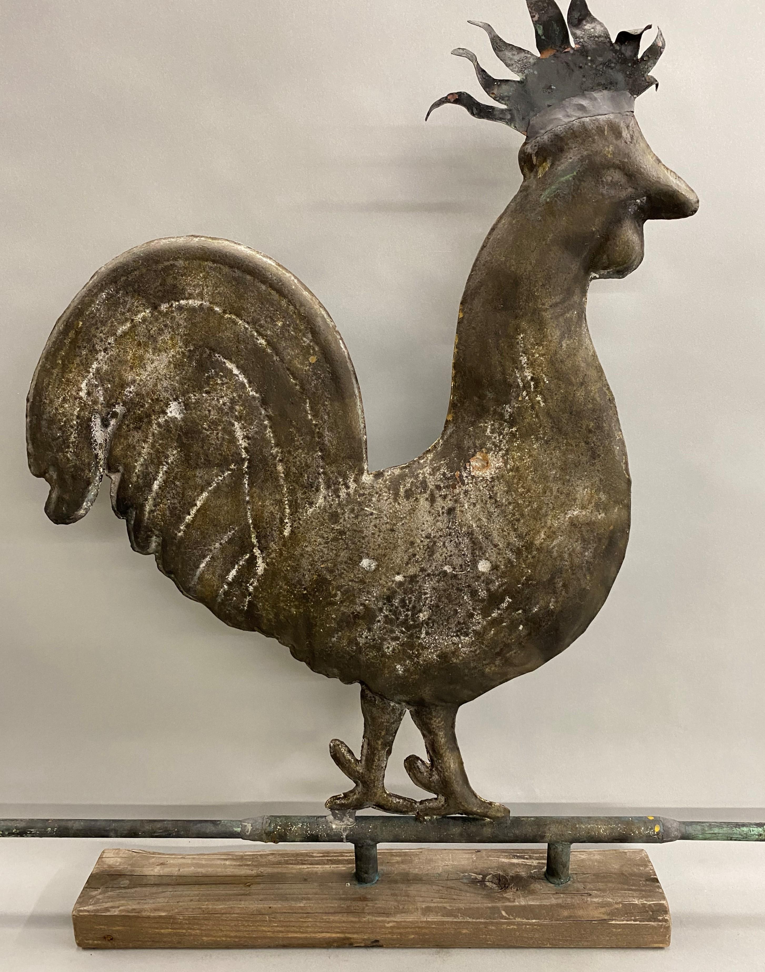 A fine example of a molded copper hollow body rooster weathervane on directional arrow, mounted on a weathered wooden display base, with nice detail on the arrow feathers and body structure. Dates to the 19th century in very good condition, with