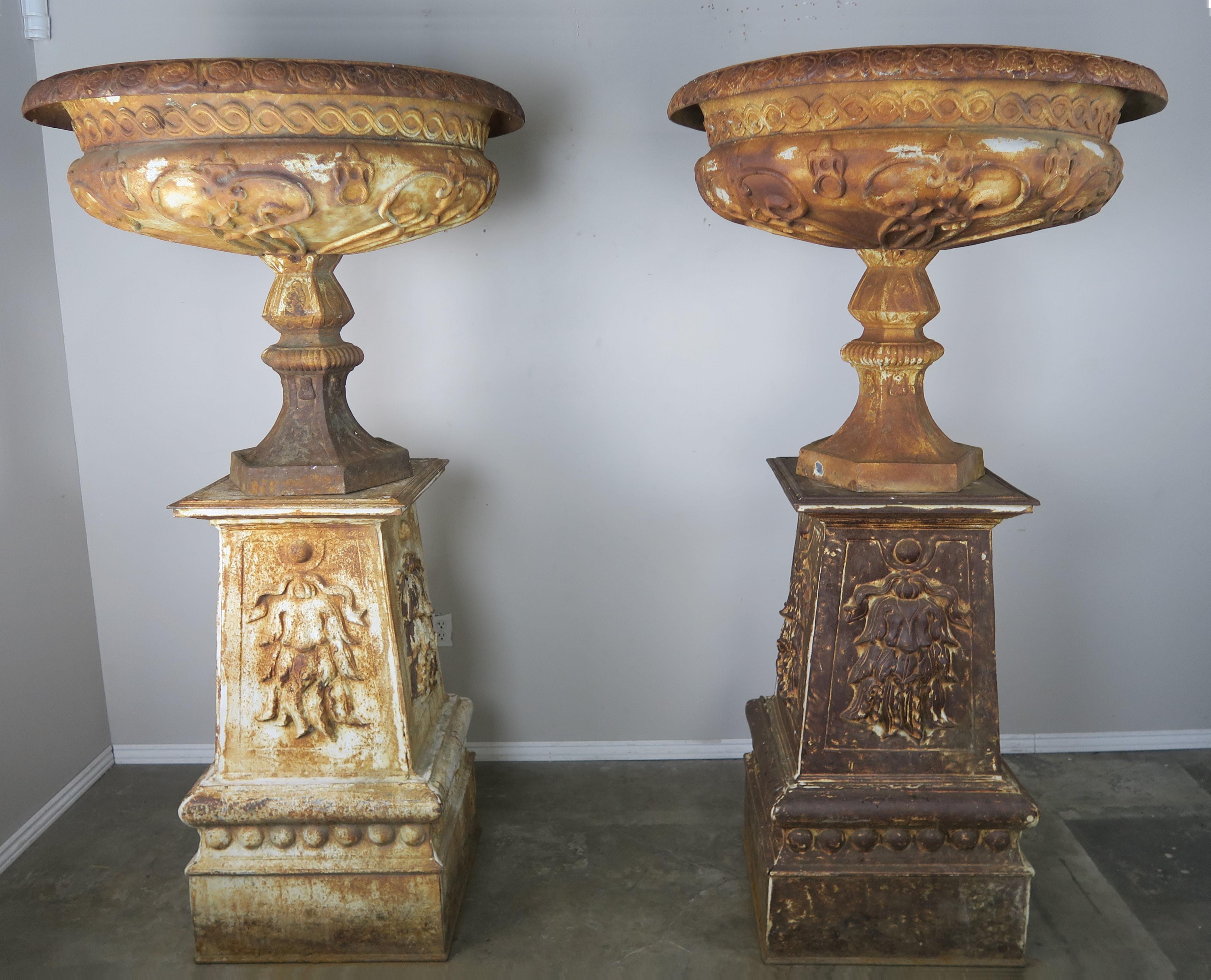 Pair of 19th century Art Nouveau style monumental French cast iron urns on original cast iron bases. The urns are beautifully decorated with floral and geometric pattern designs throughout. The urns have a great patina-missing paint throughout and