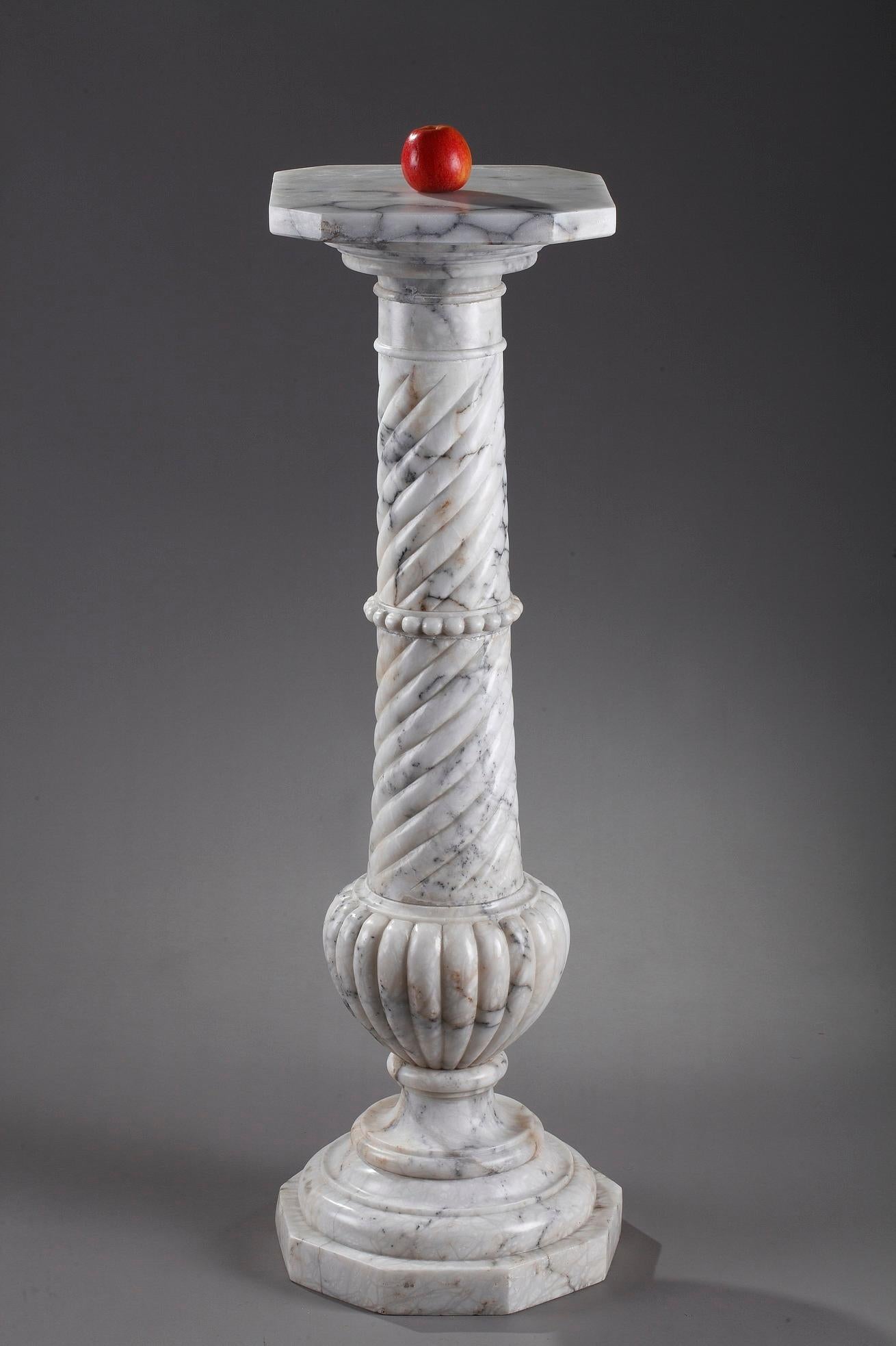 Large spiraling column pedestal stand with Doric capital. The pedestal is crafted in richly veined white marble with a rotating display plate. The marble pedestal is decorated with a frieze of pearls and rests on a base with multiple terraced,