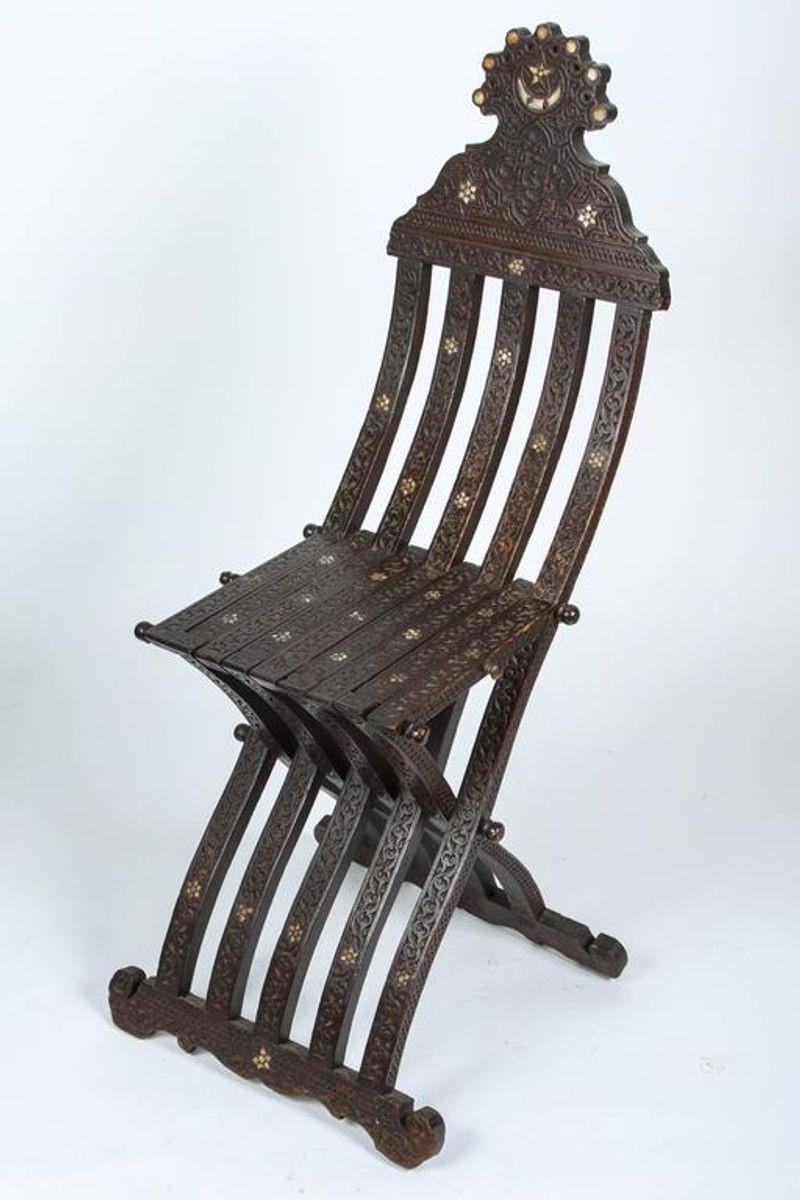 Middle Eastern Moorish wood folding chair with intricate foliate carving and mother-of-pearl inlays.
Inlaid with mother-of-pearl stars and moon designs, hand-carved with Arabic calligraphy and foliages.
Some mother-of-pearl inlay missing, great